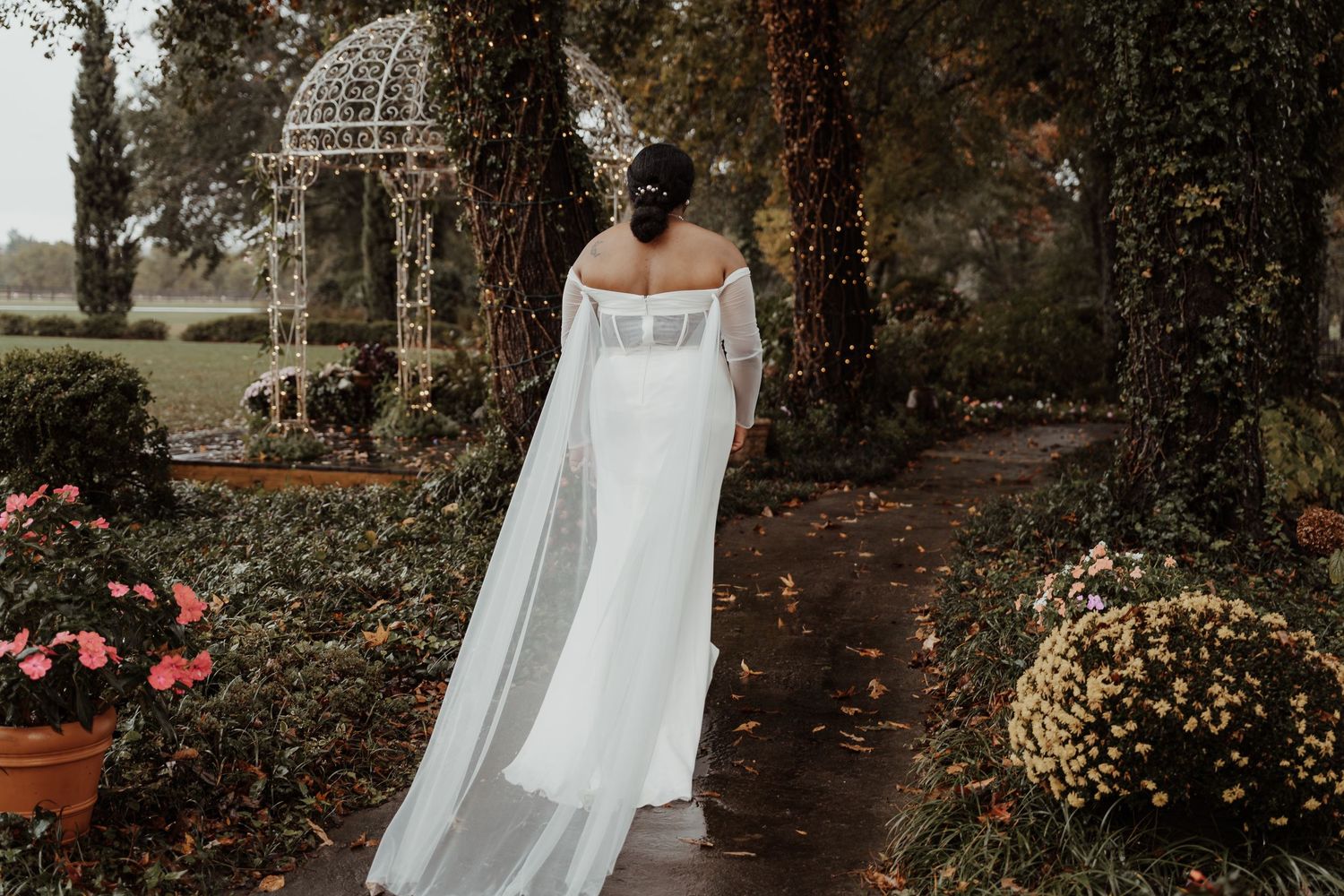 An elegant wedding dress with flowing train in a garden setting with gazebo.
