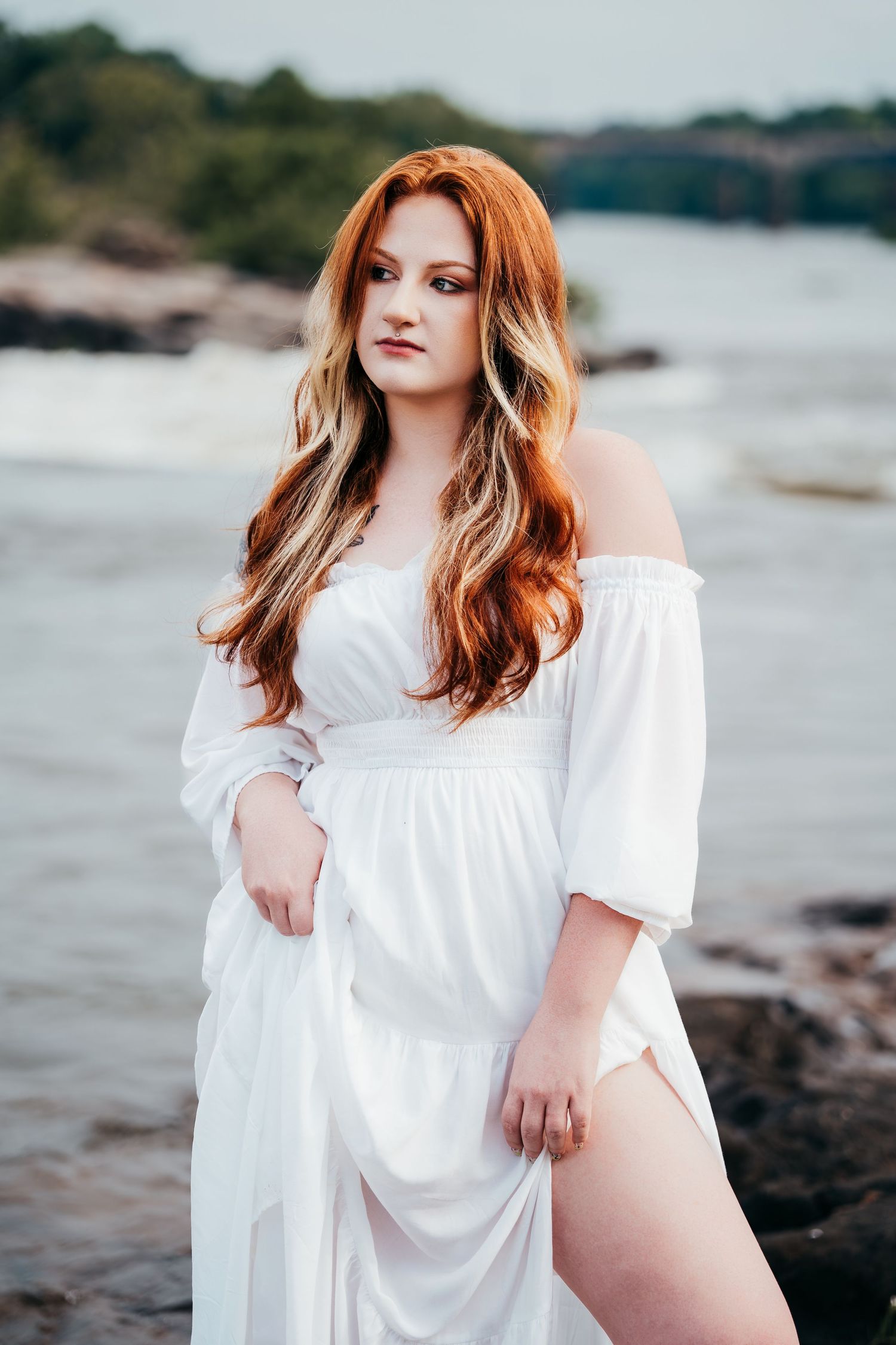 Portrait session in white flowing dress at rocky beach shoreline with moody ocean backdrop.