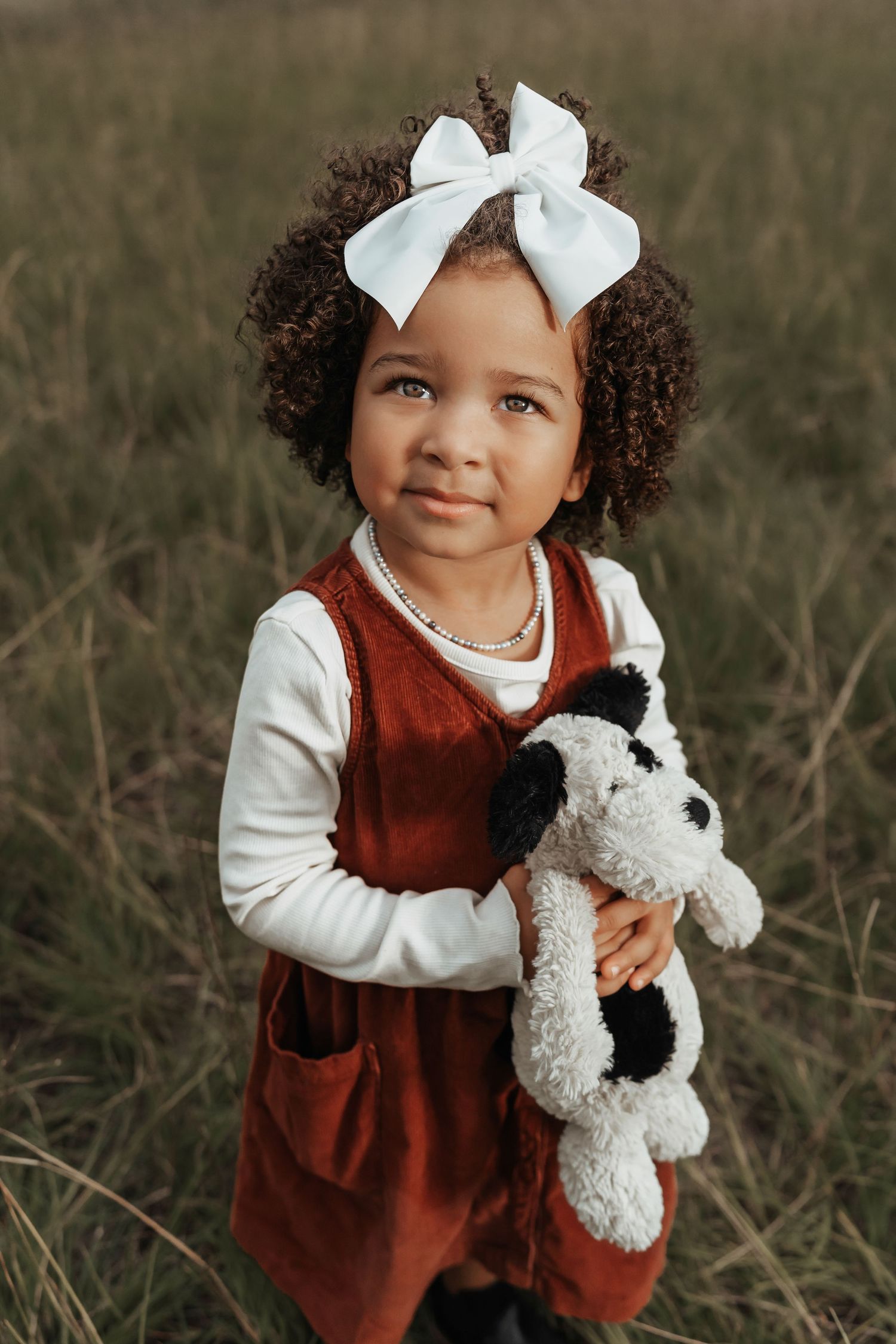 Young child in red corduroy dress holding stuffed animal outdoors.