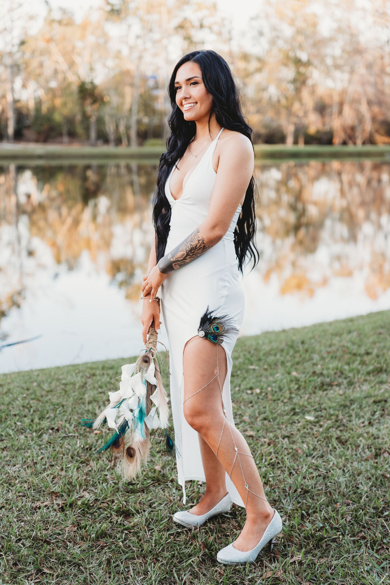 Elegant bride in white dress poses by lakeside during golden hour.