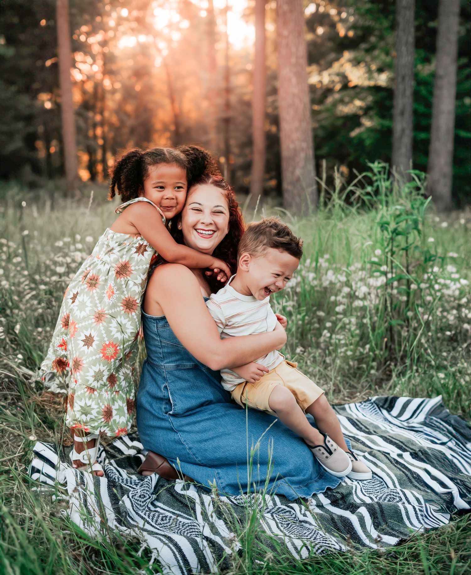 Family enjoying a sunset picnic in a meadow while sitting on a striped blanket among wildflowers.