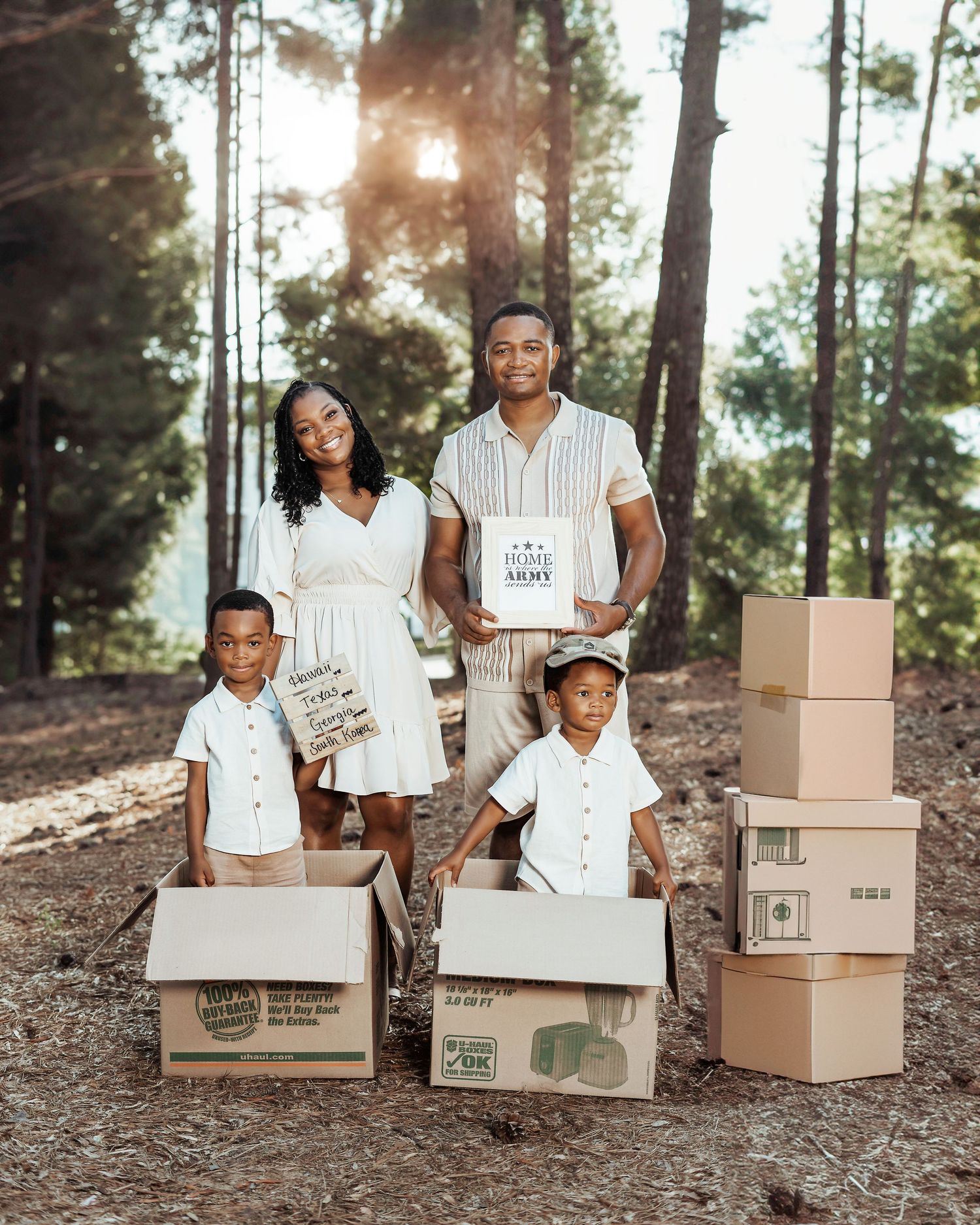 A family stands with moving boxes in a beautiful wooded setting with sun rays filtering through the pine trees.
