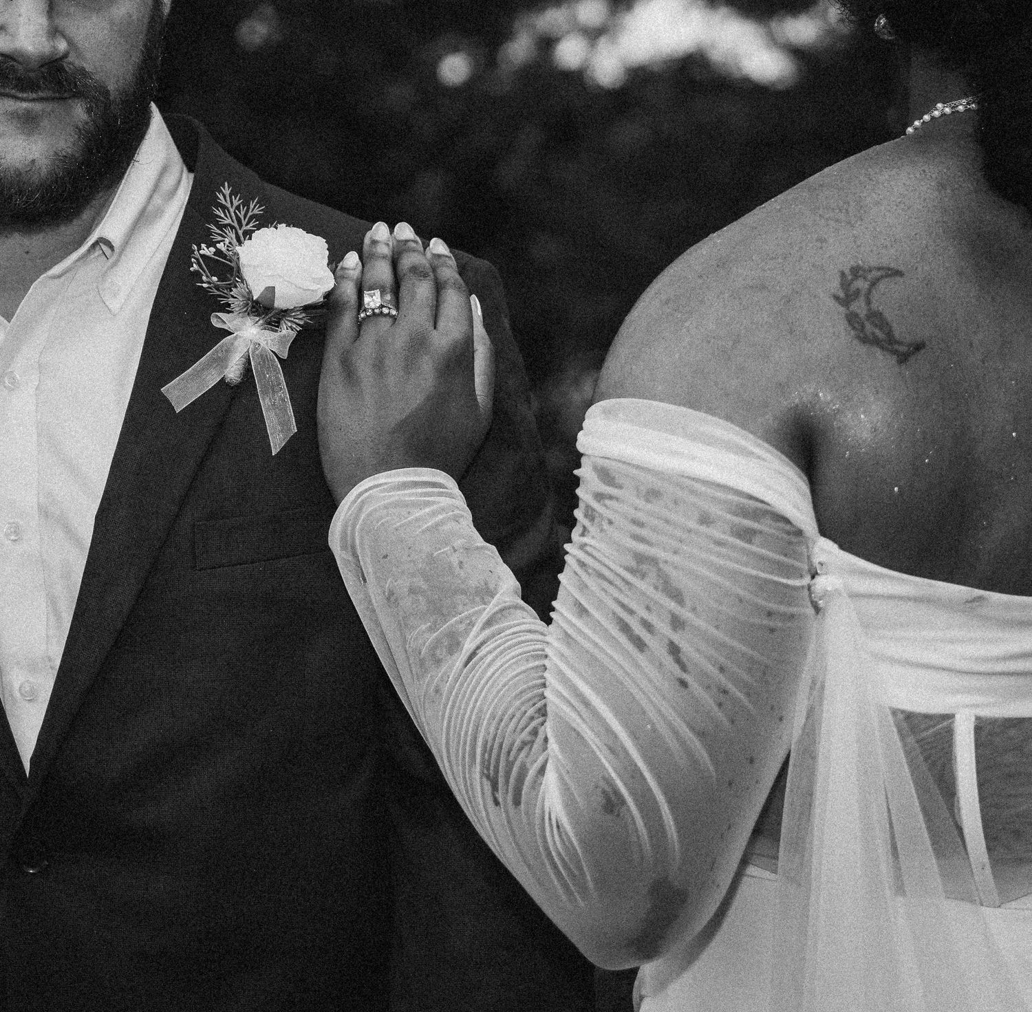 Close up detail of elegant wedding attire showing hands, rings, and a boutonniere.
