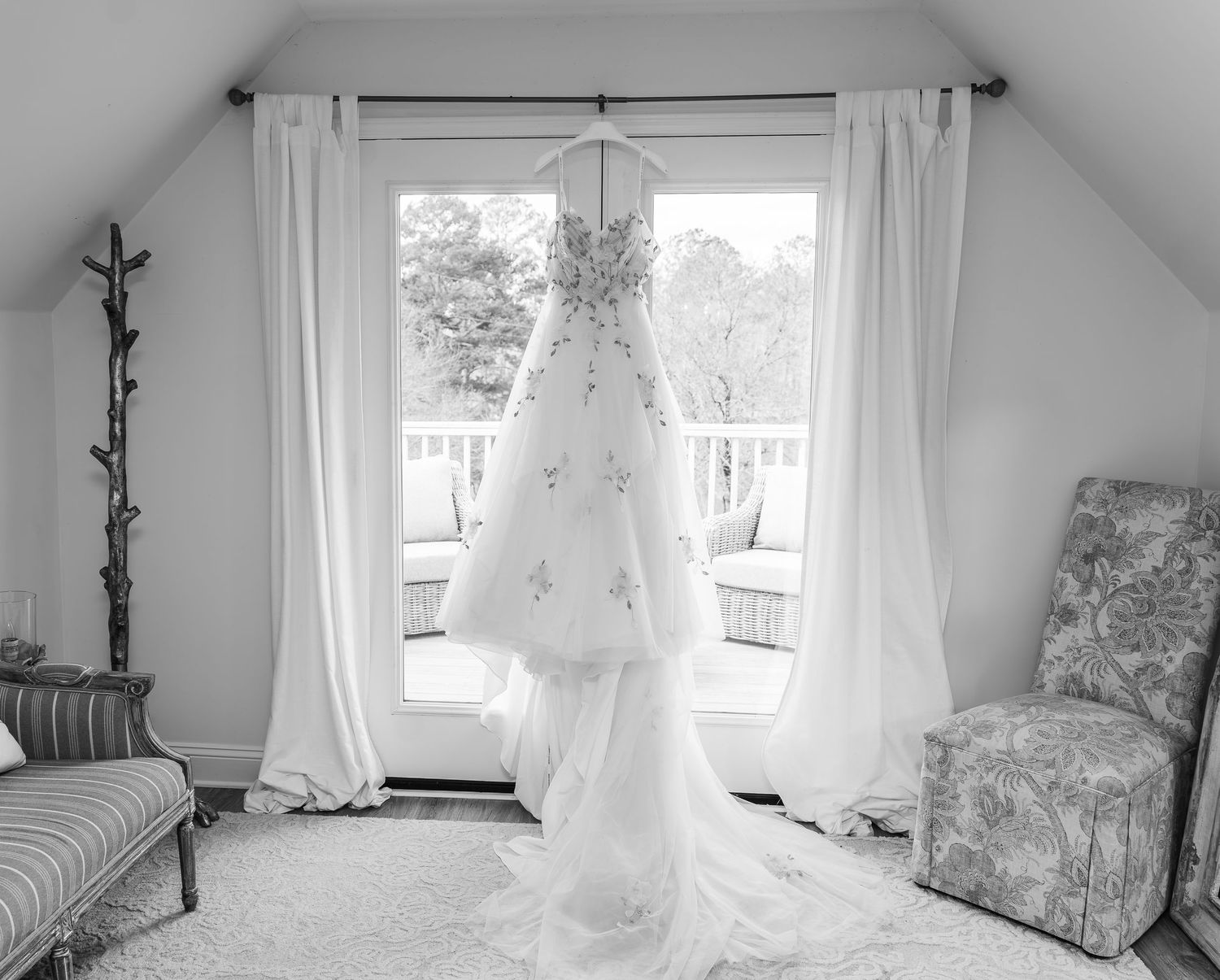 Delicate white wedding dress hanging in window of bright, minimalist bridal suite.