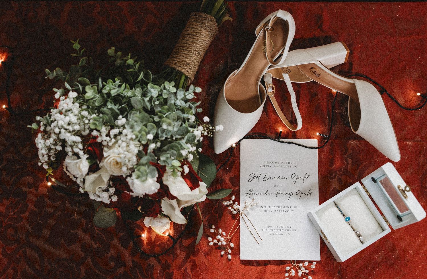 Wedding details flatlay with white shoes, floral bouquet and invitation on red background.