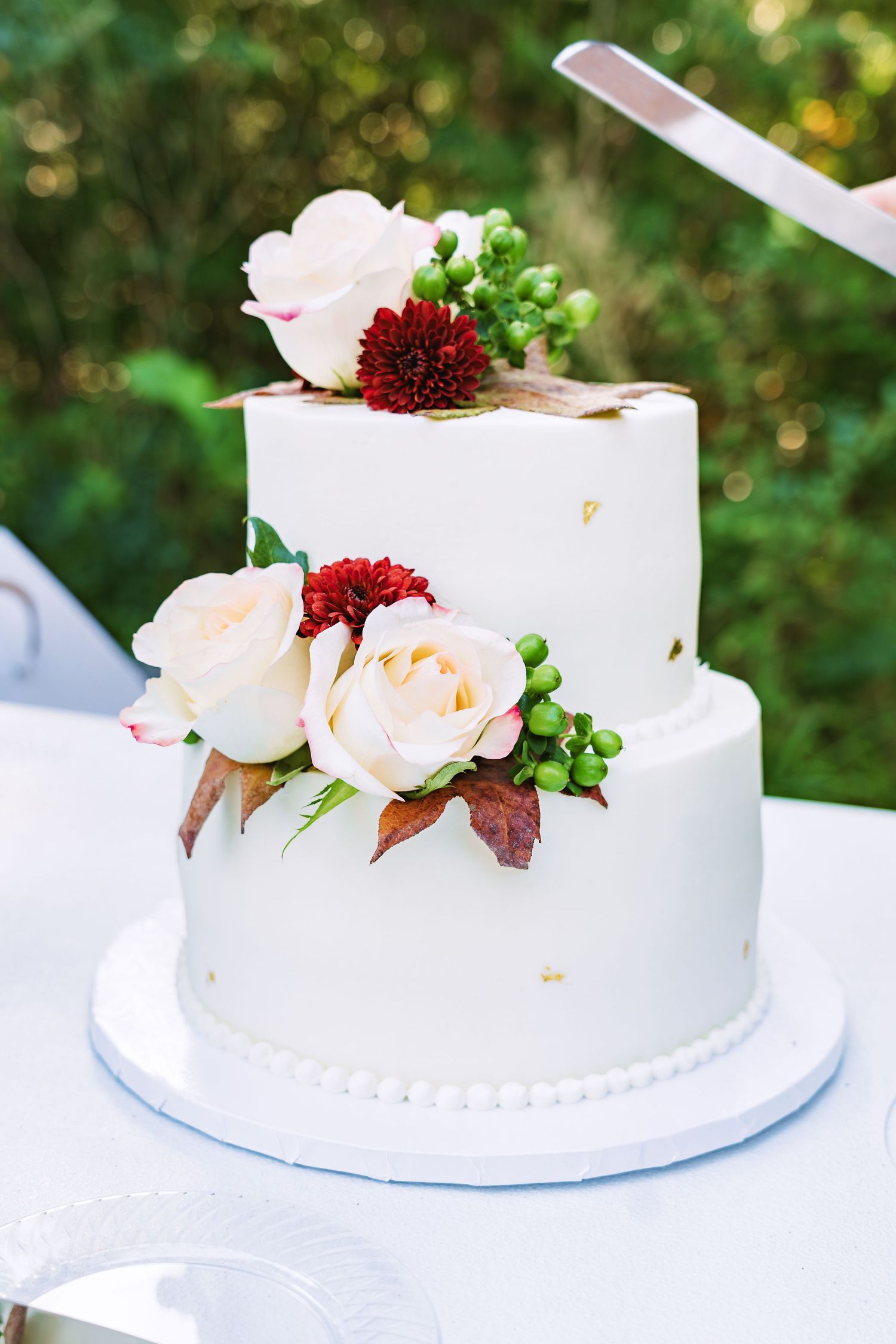 Elegant two-tier white wedding cake decorated with blush roses and burgundy flowers.