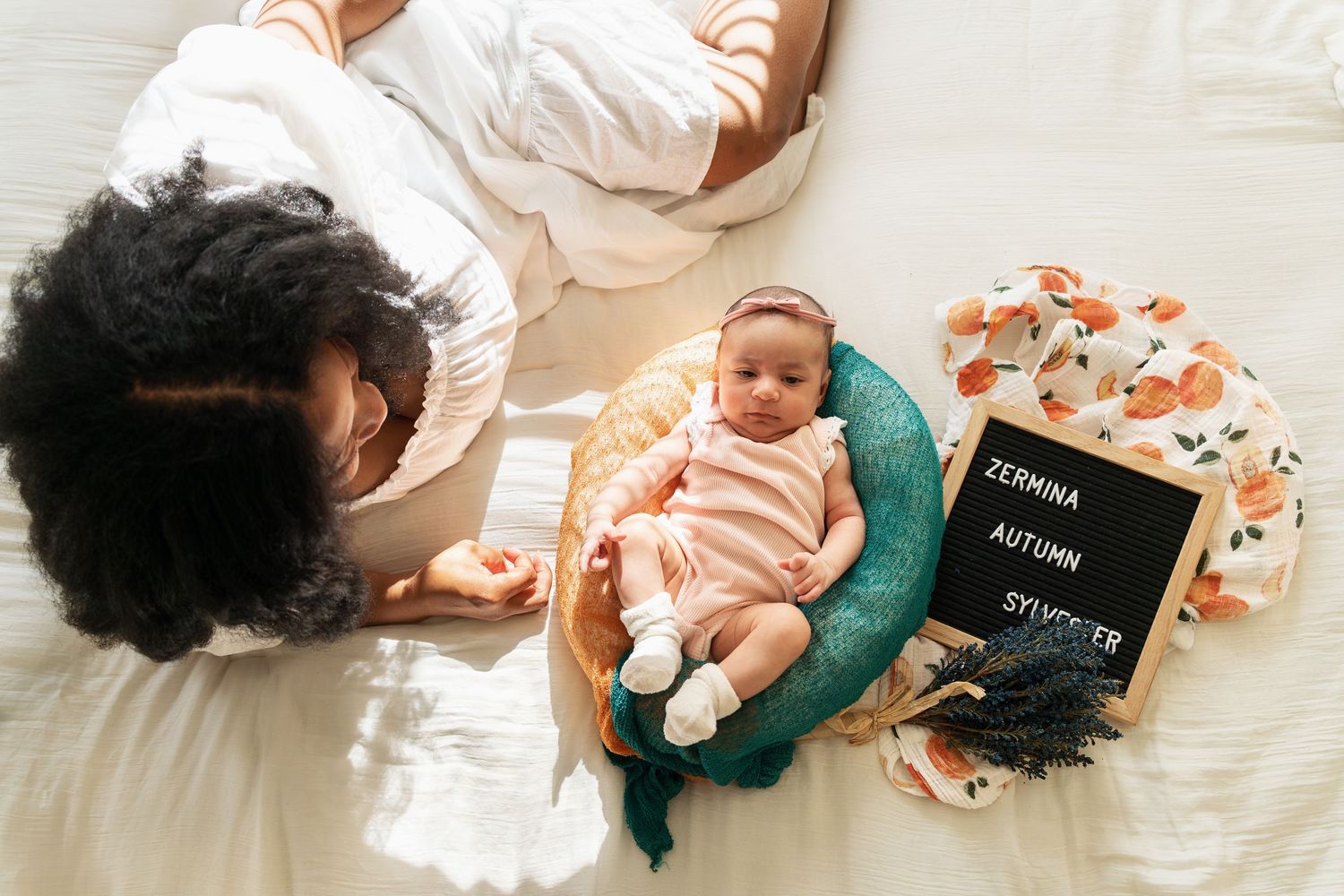 Mother and infant on bed with letter board and decorative items for milestone photo.