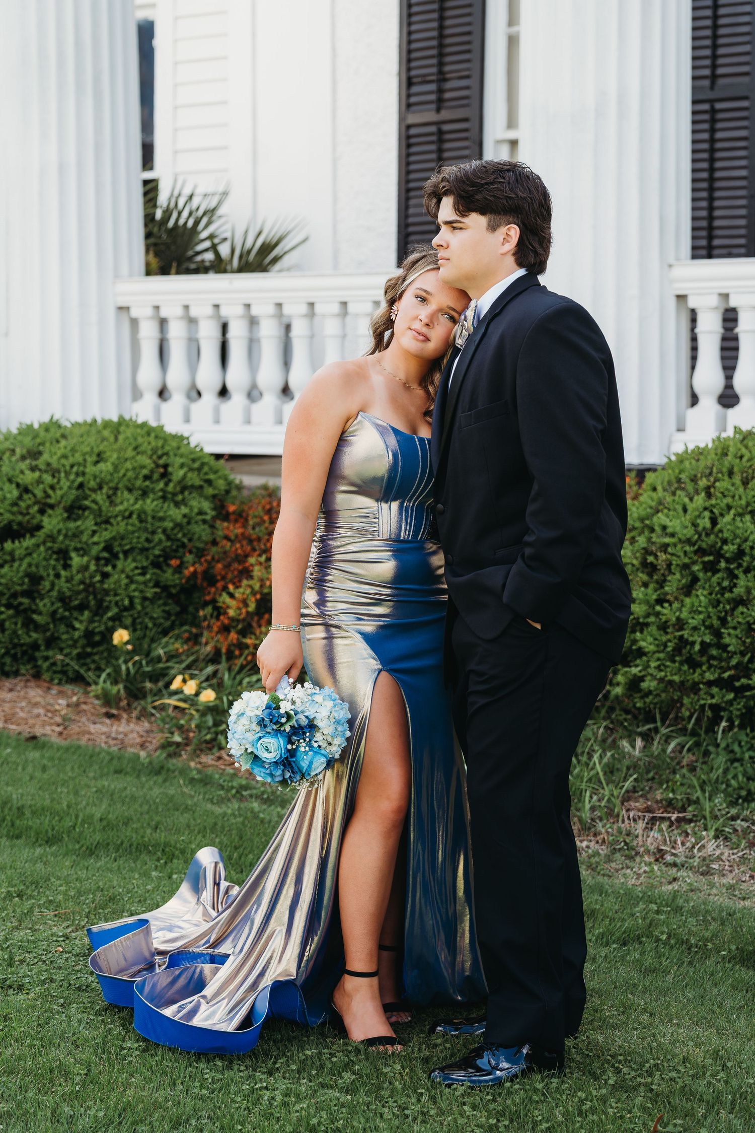 Couple in formal attire poses for prom photos in front of white columned building.