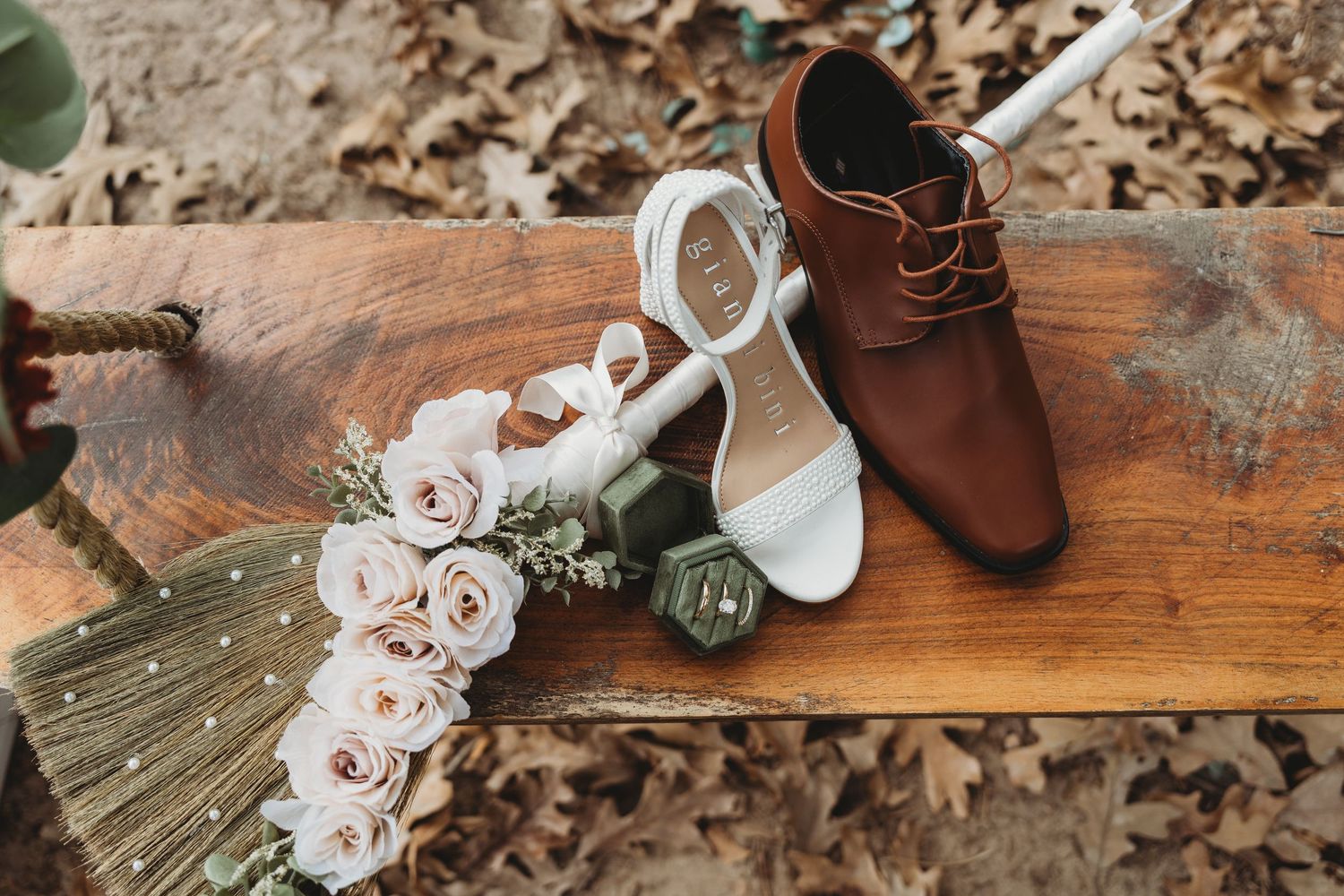 Wedding shoes and bridal bouquet with white orchids arranged on wooden surface with autumn leaves.