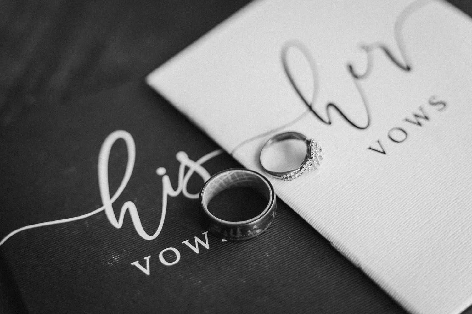 Wedding rings displayed on black and white vow book with cursive lettering.