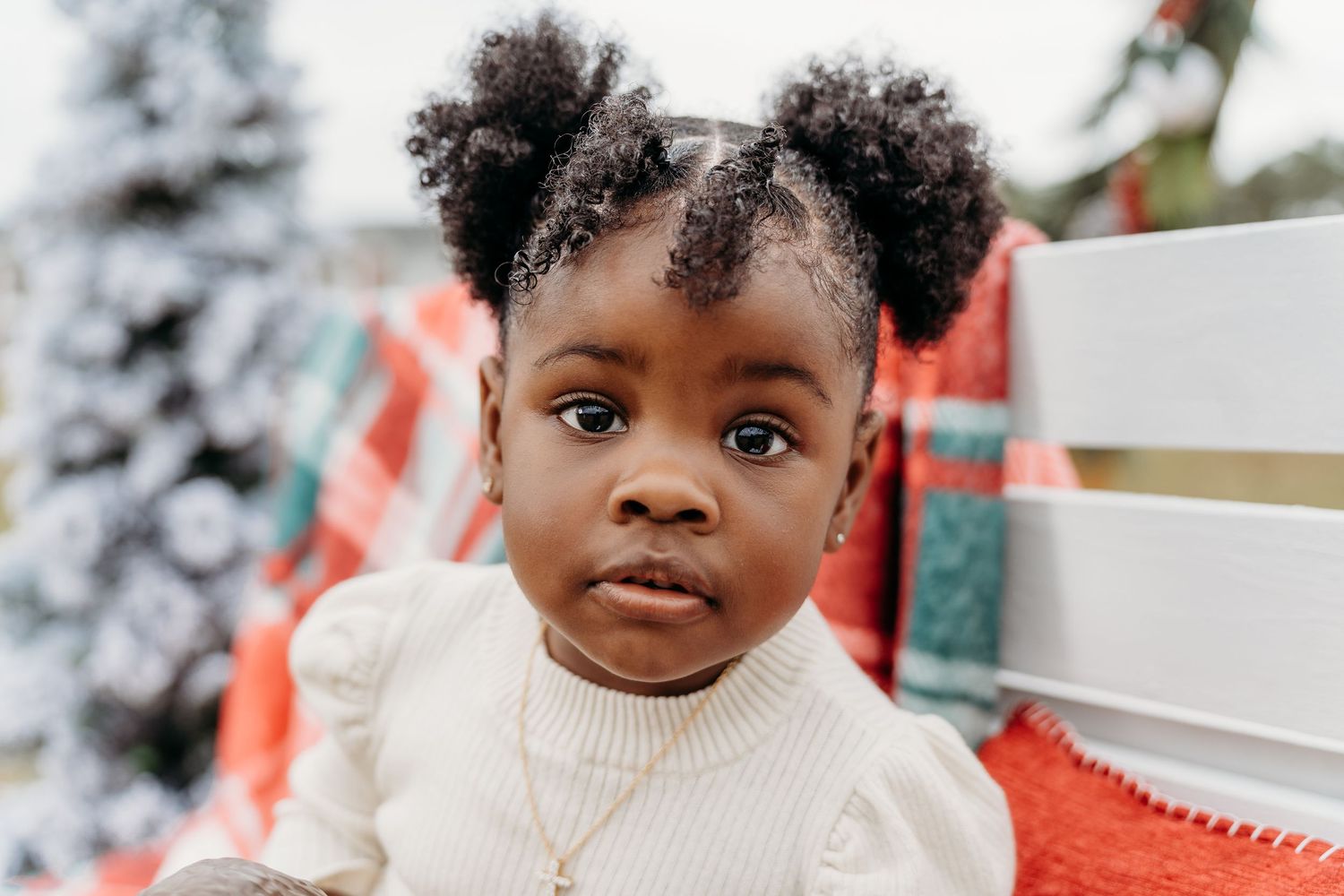 A small child in a cream sweater seated in front of winter holiday decorations.