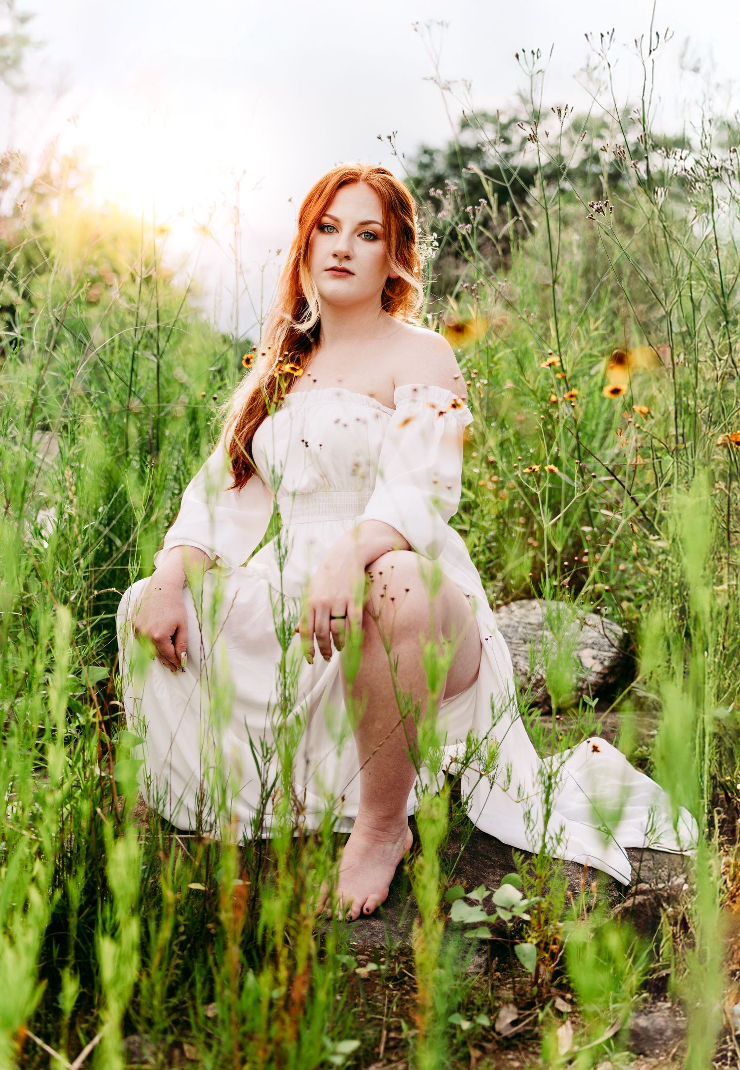 A dreamy portrait in a wildflower meadow features a white summer dress and long braided hair against soft natural lighting.