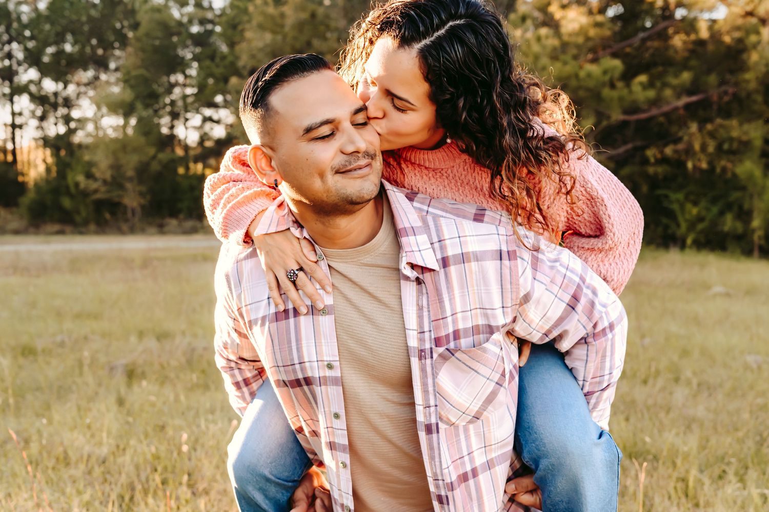 A couple sharing a playful piggyback ride moment in an open field at sunset.