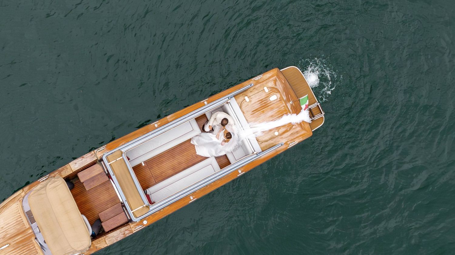 Aerial view of a luxury yacht with wooden deck and white exterior cruising through dark turquoise waters.