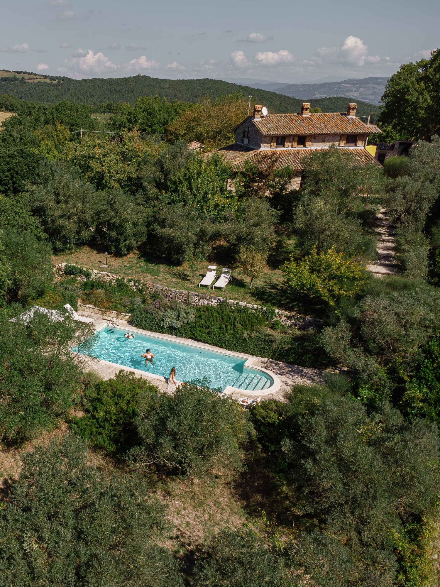 Aerial view of a rustic villa with swimming pool nestled in the Tuscan countryside surrounded by lush greenery.