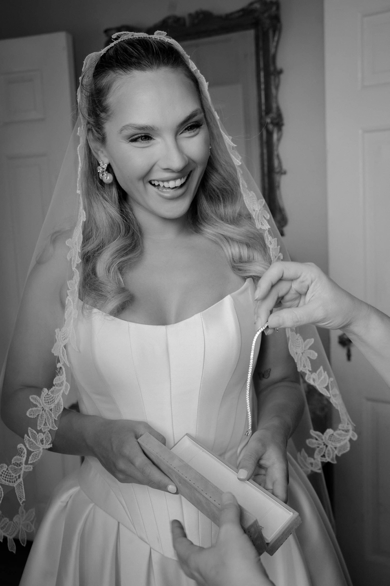 Black and white photos of a bride getting ready in a white wedding dress with a delicate lace veil.