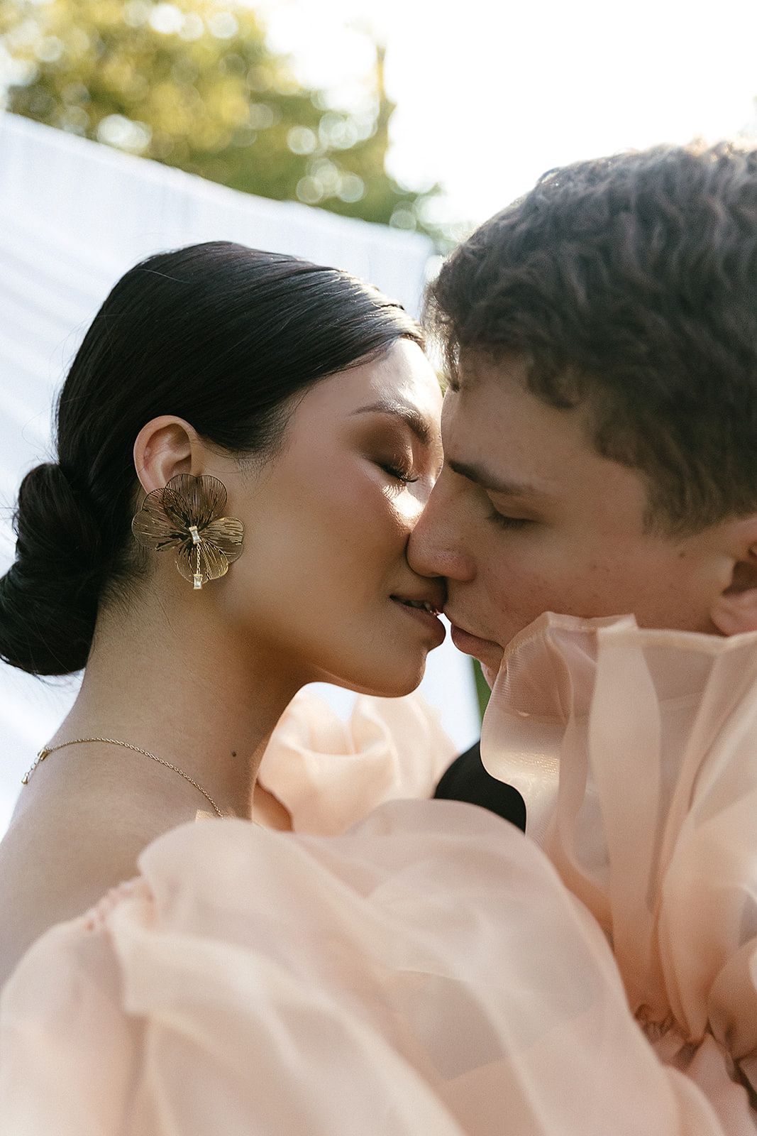A romantic close-up sequence of a couple sharing an intimate kiss, with a soft pink veil surrounding them.