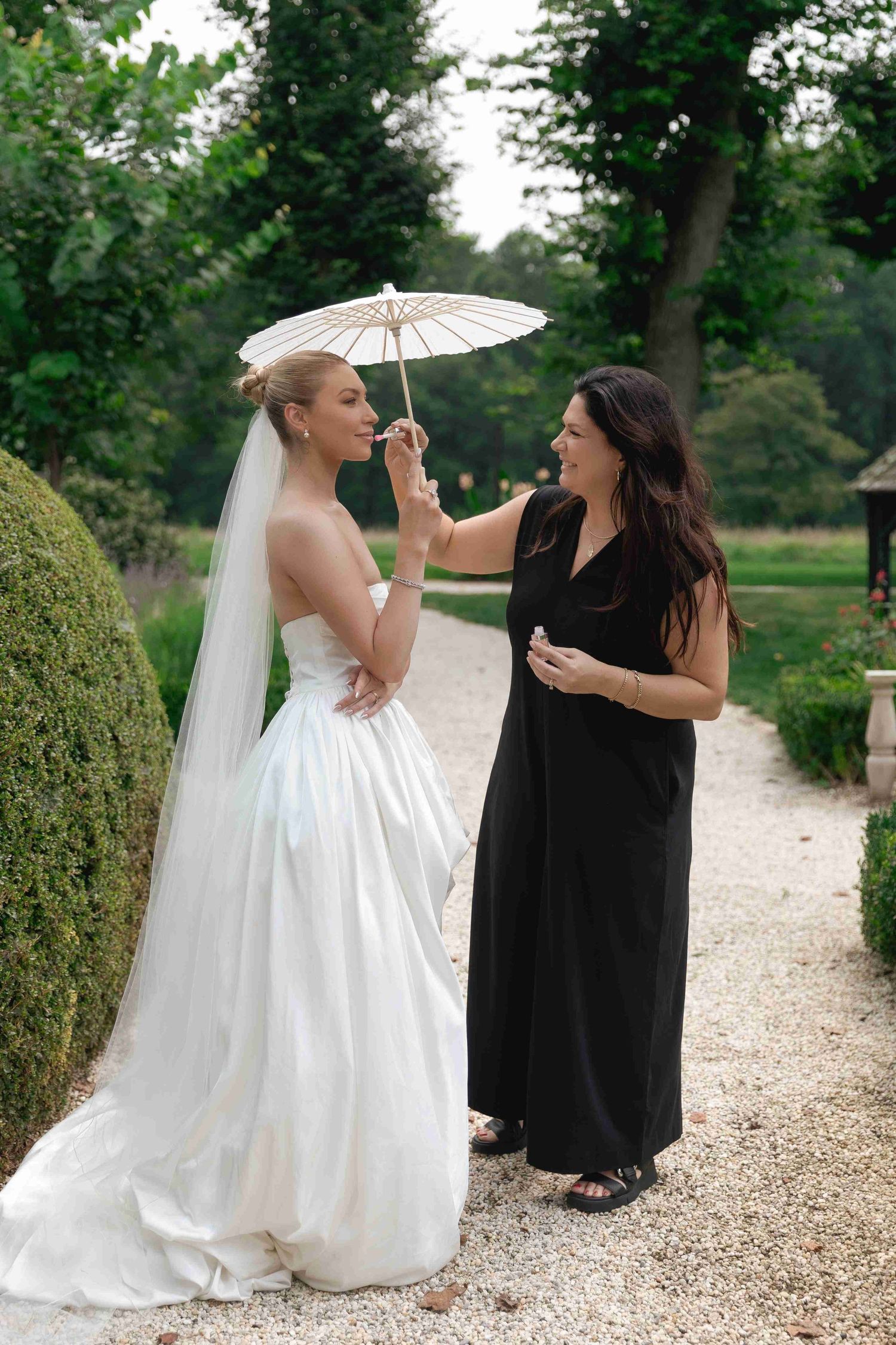 Two people in contrasting black and white outfits share a joyful moment on a gravel path surrounded by greenery.