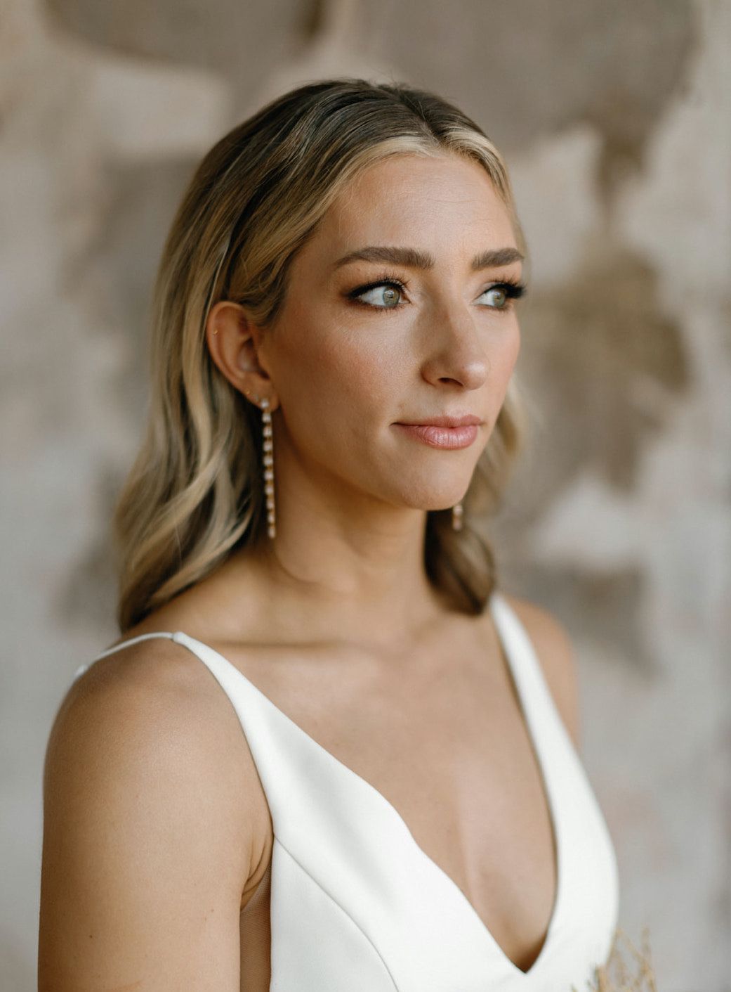 A bride in a white wedding dress poses elegantly against a soft neutral background.