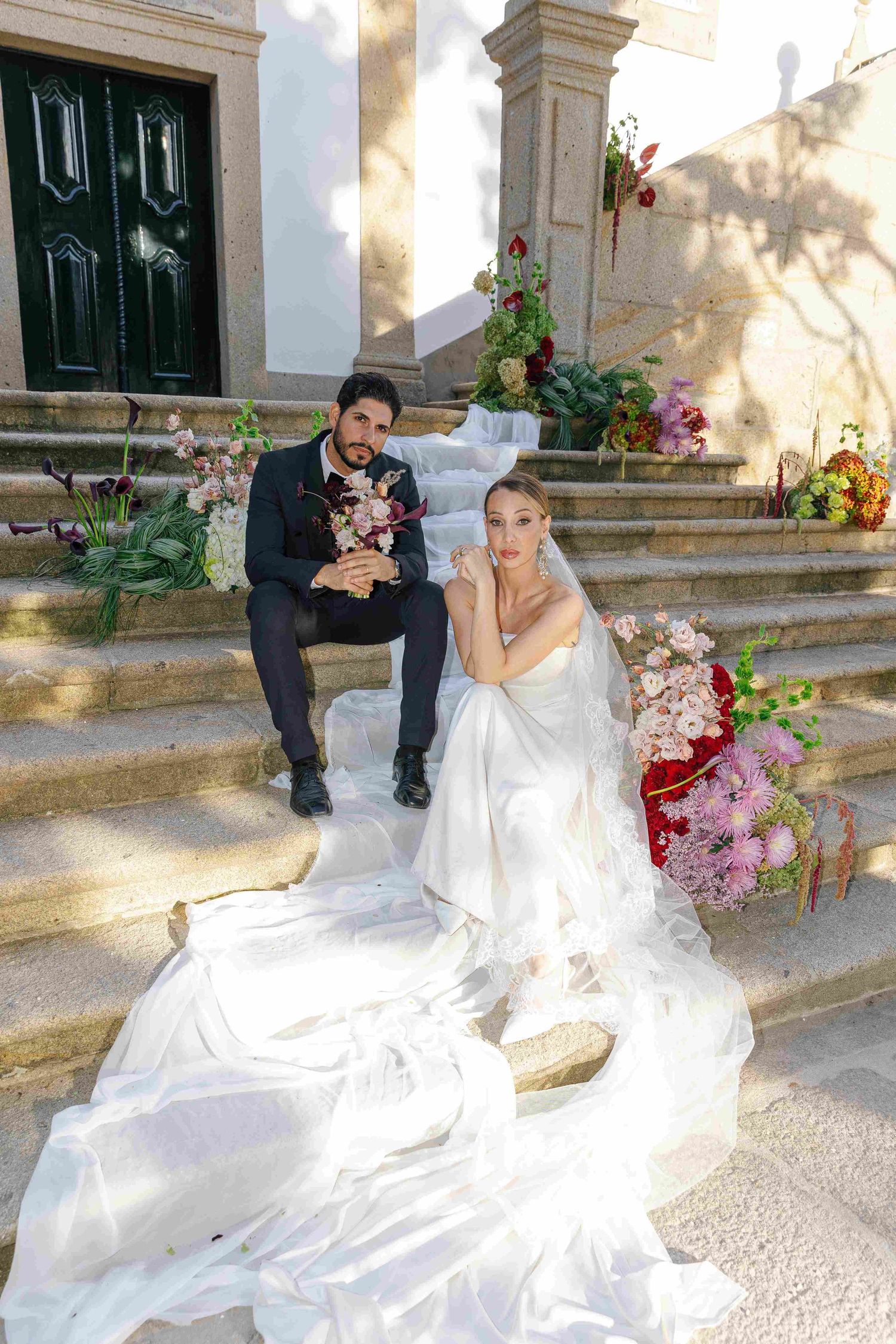 Romantic wedding photos on stone steps with a bride in a flowing white gown and floral arrangements.