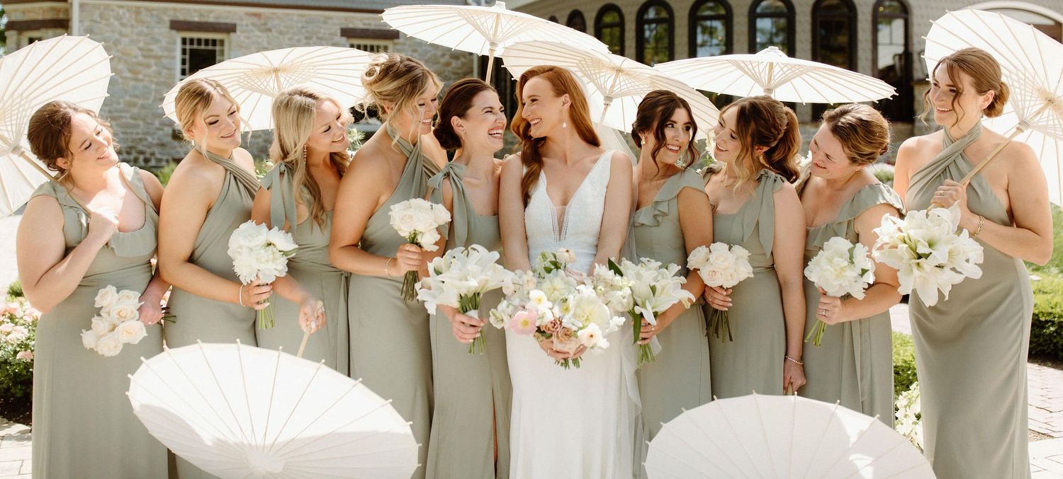 Wedding party poses in a row wearing sage green dresses and holding pink and white floral bouquets.