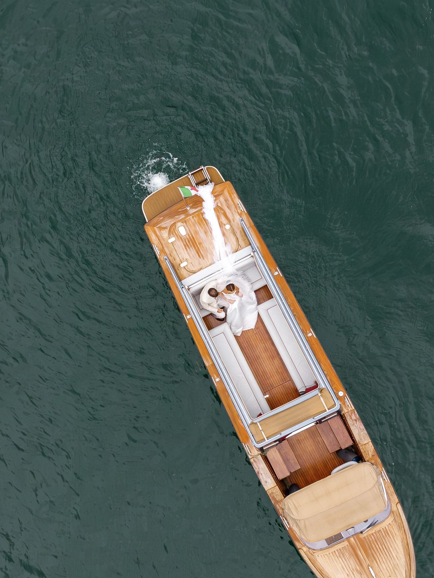 Aerial view of newlyweds on a wooden boat in turquoise waters.