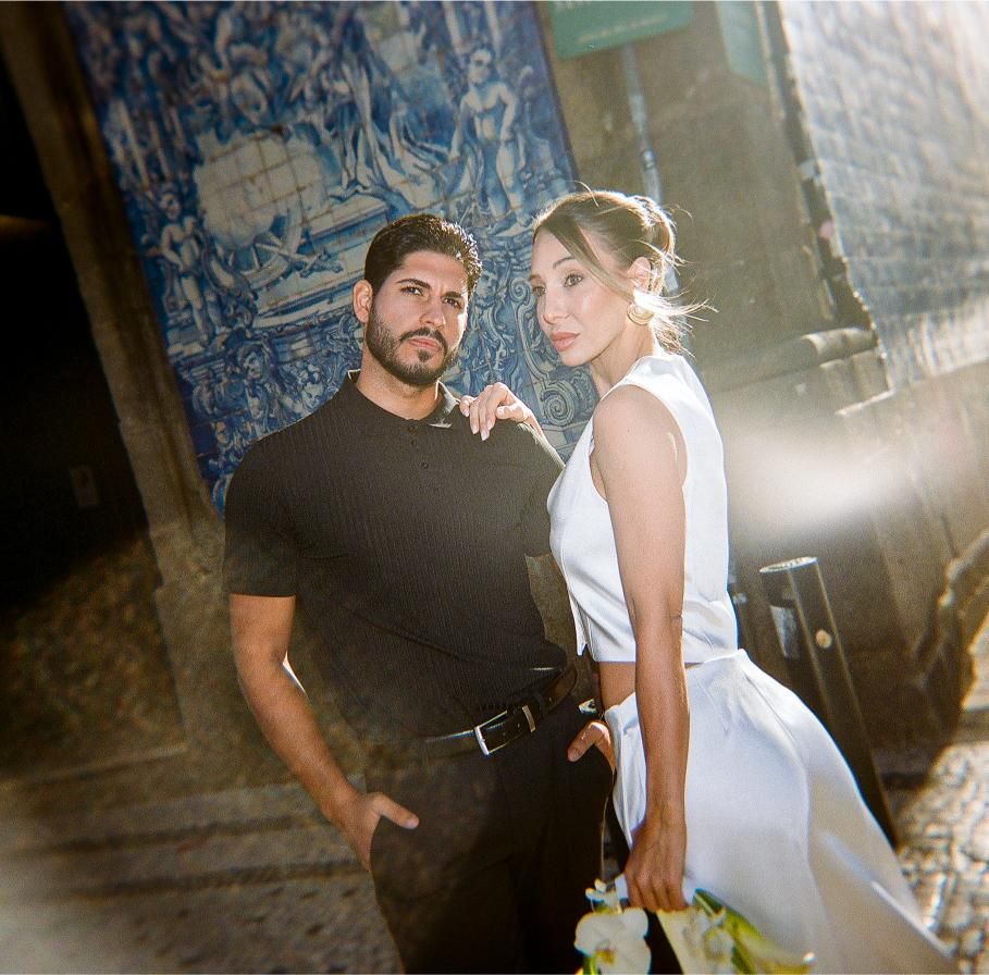 A couple in romantic poses during an engagement photo session against a textured wall with natural lighting.