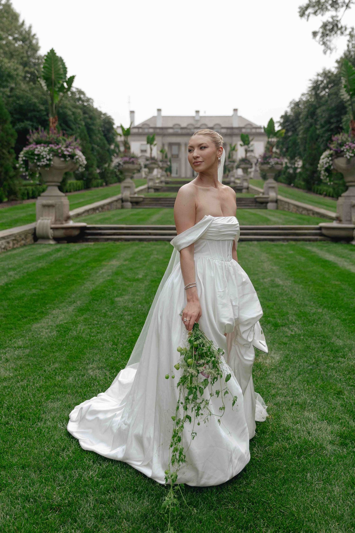 An elegant white dress flows across manicured lawns with a grand estate in the background.