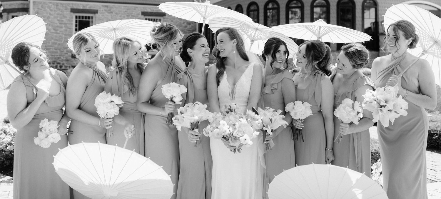 A black and white panoramic photo shows a wedding party posing together outdoors in formal attire.