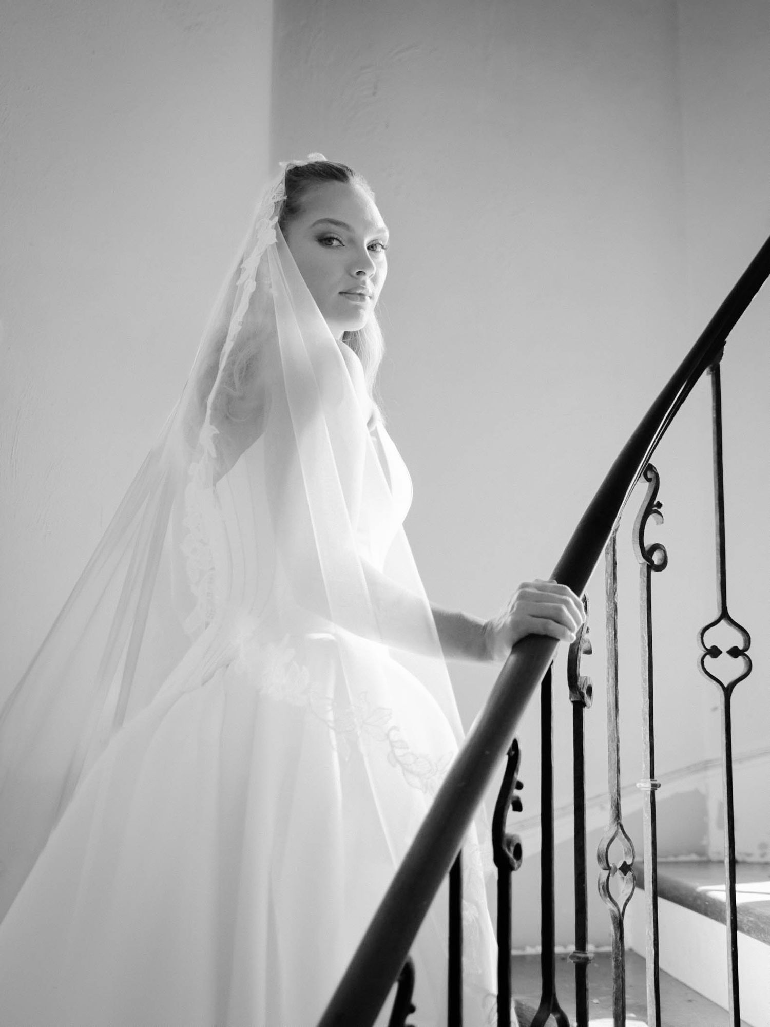 Black and white photos of a bride in flowing veil ascending a staircase with ornate iron railings.