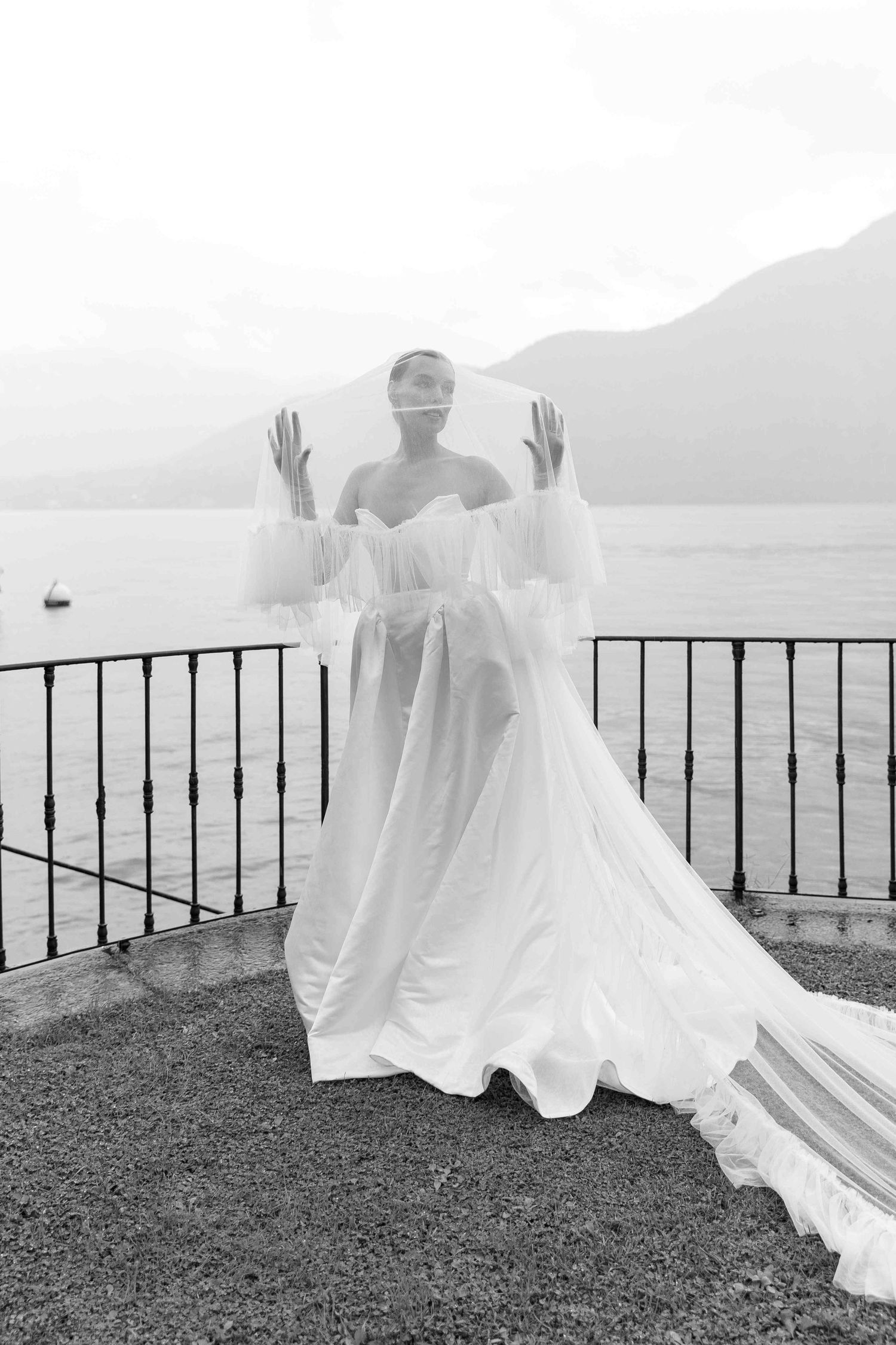 Bride in flowing white dress poses against scenic mountain and lake backdrop.