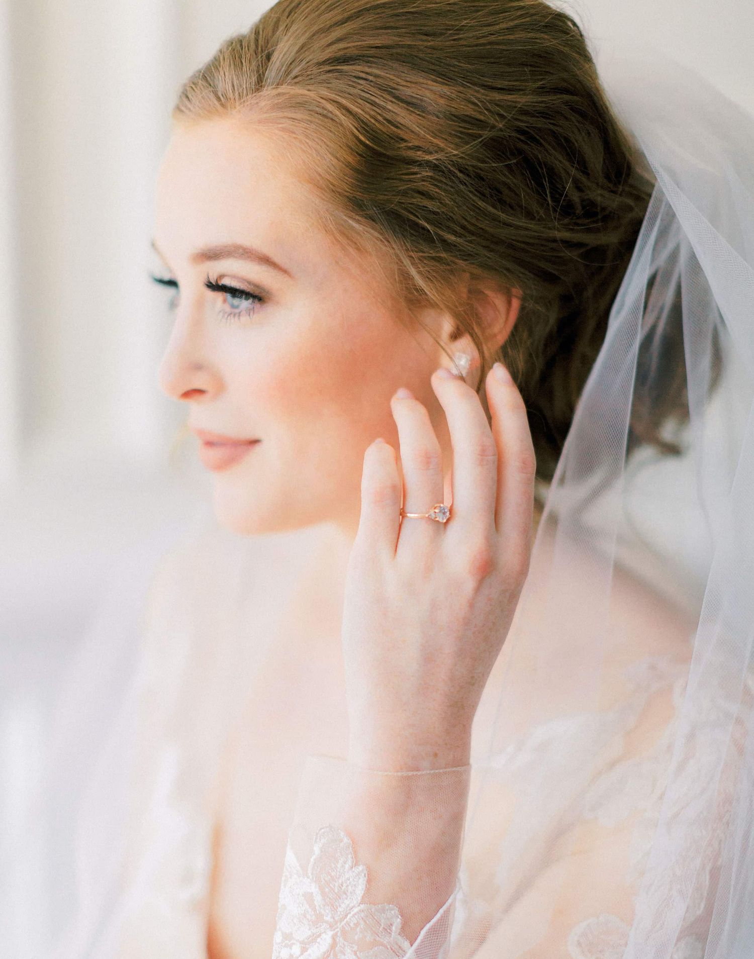 Elegant bride in soft focus wearing a delicate veil and diamond earrings in ethereal natural light.