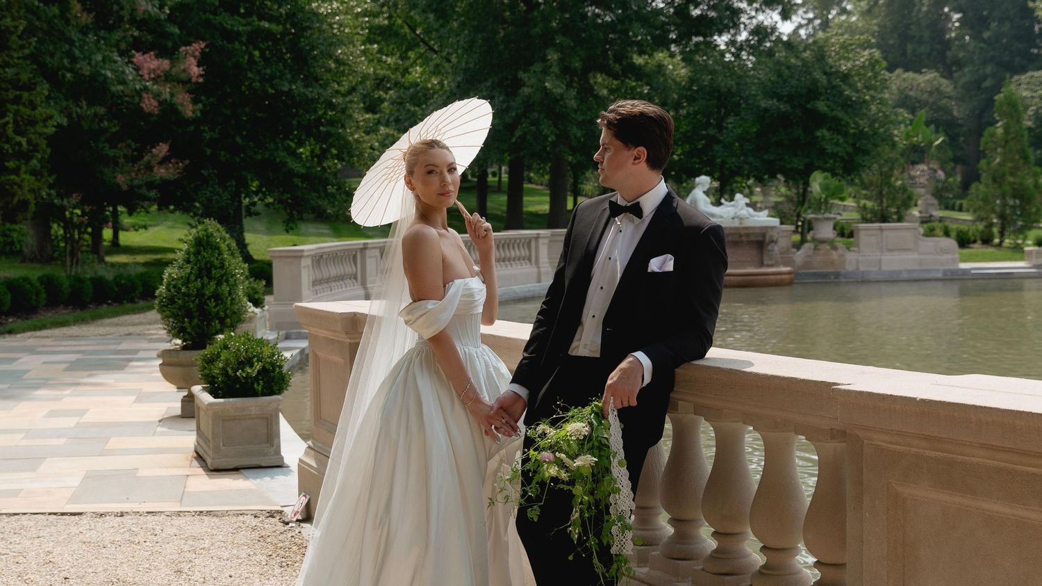 A romantic wedding photoshoot on a grand stone balcony surrounded by lush greenery and elegant architecture.