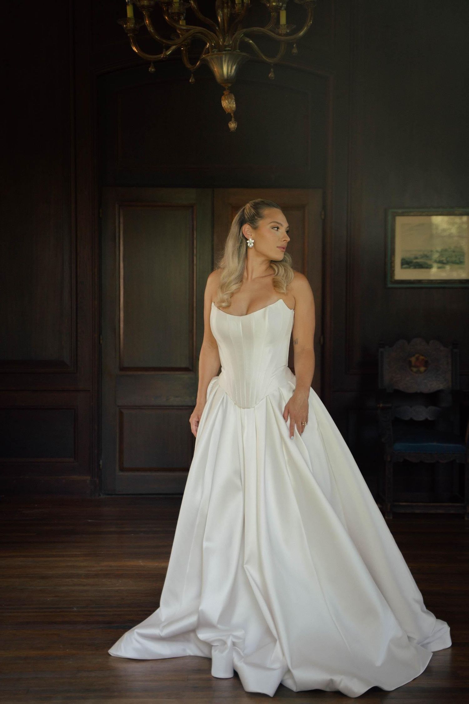 Elegant white wedding gown with dramatic full skirt displayed in a dark wood-paneled room.