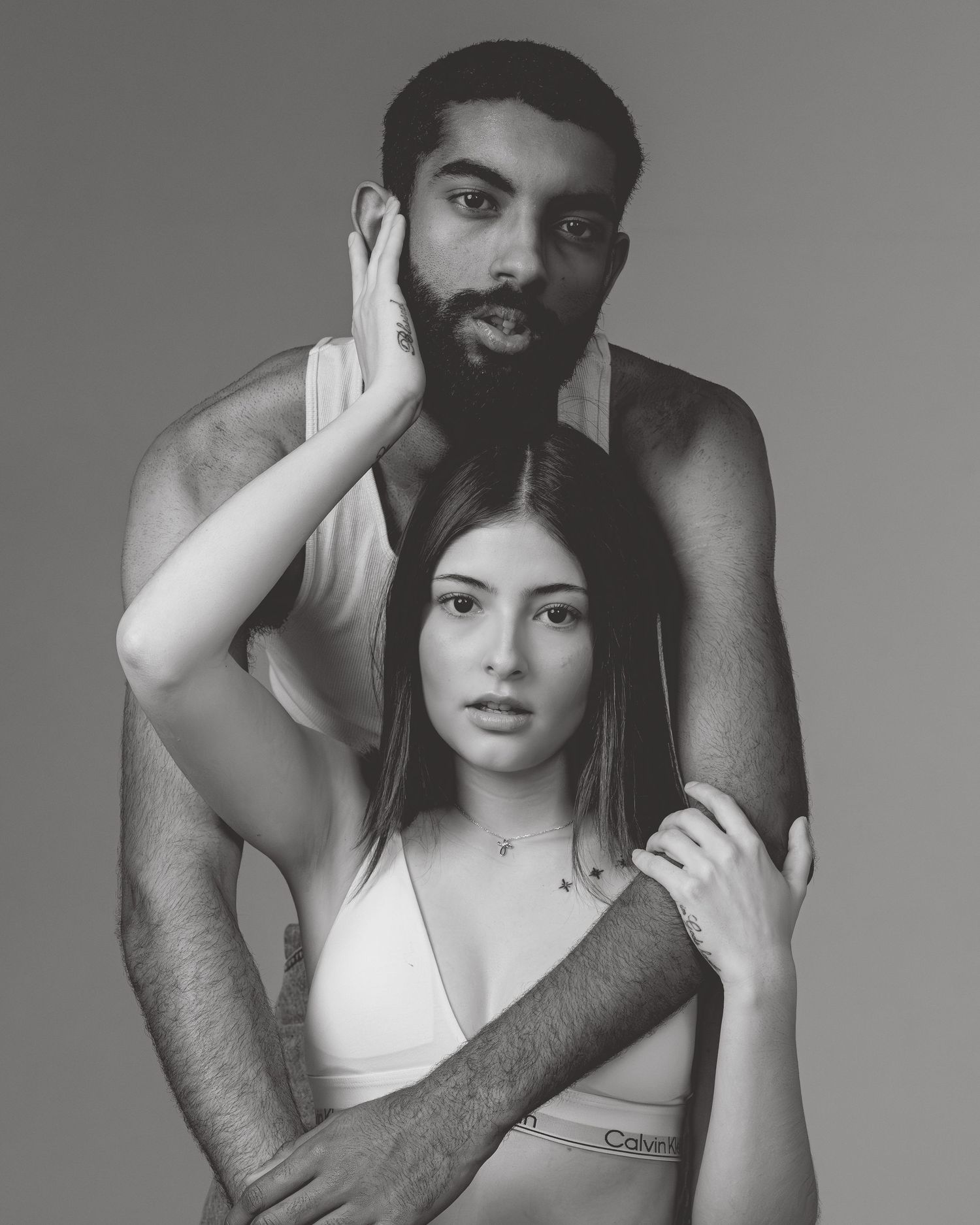 Black and white photo of a couple posing together, man standing behind woman in Calvin Klein underwear.