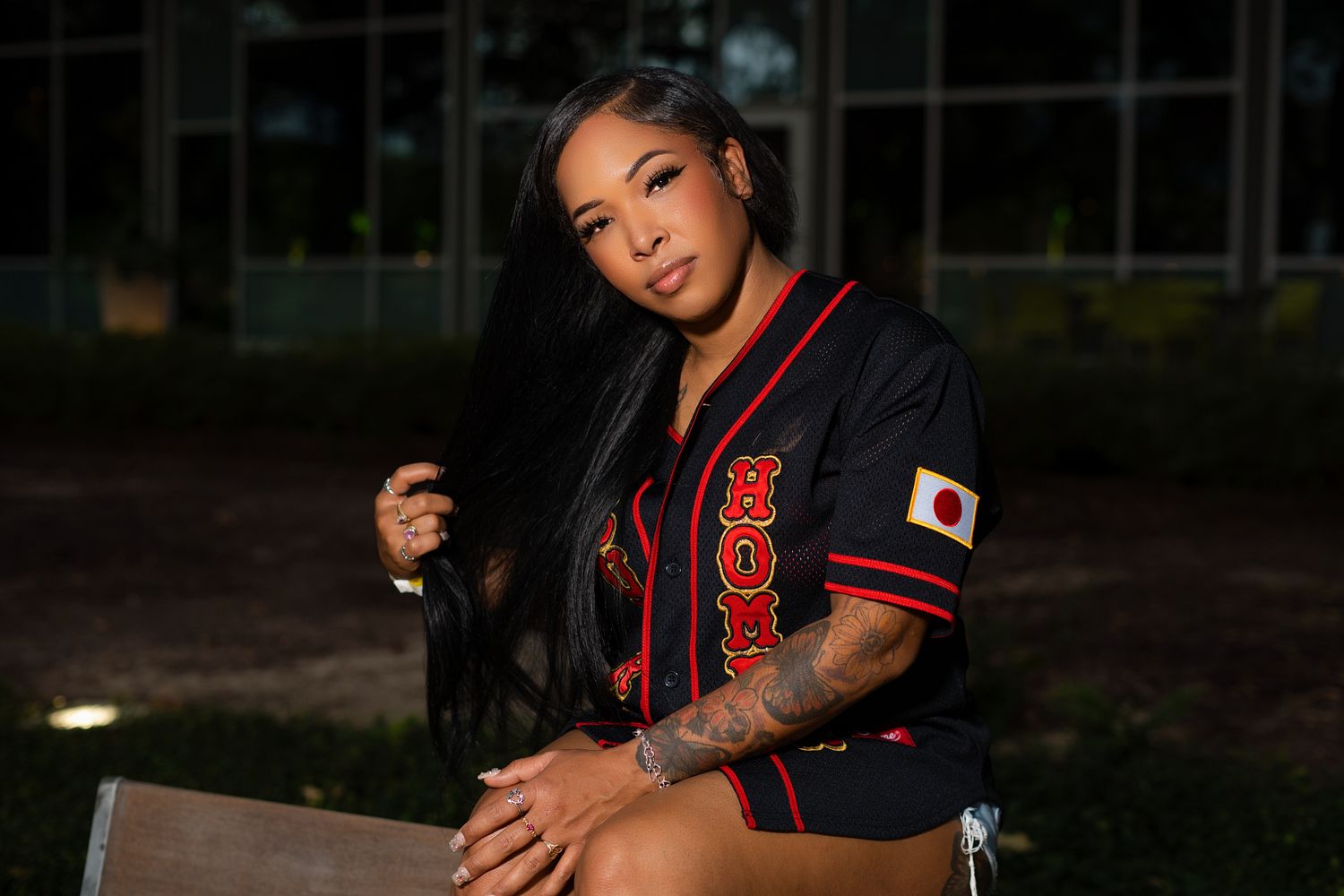 Woman in varsity-style jacket poses outdoors at dusk. Powerrpackmedia Houston Texas