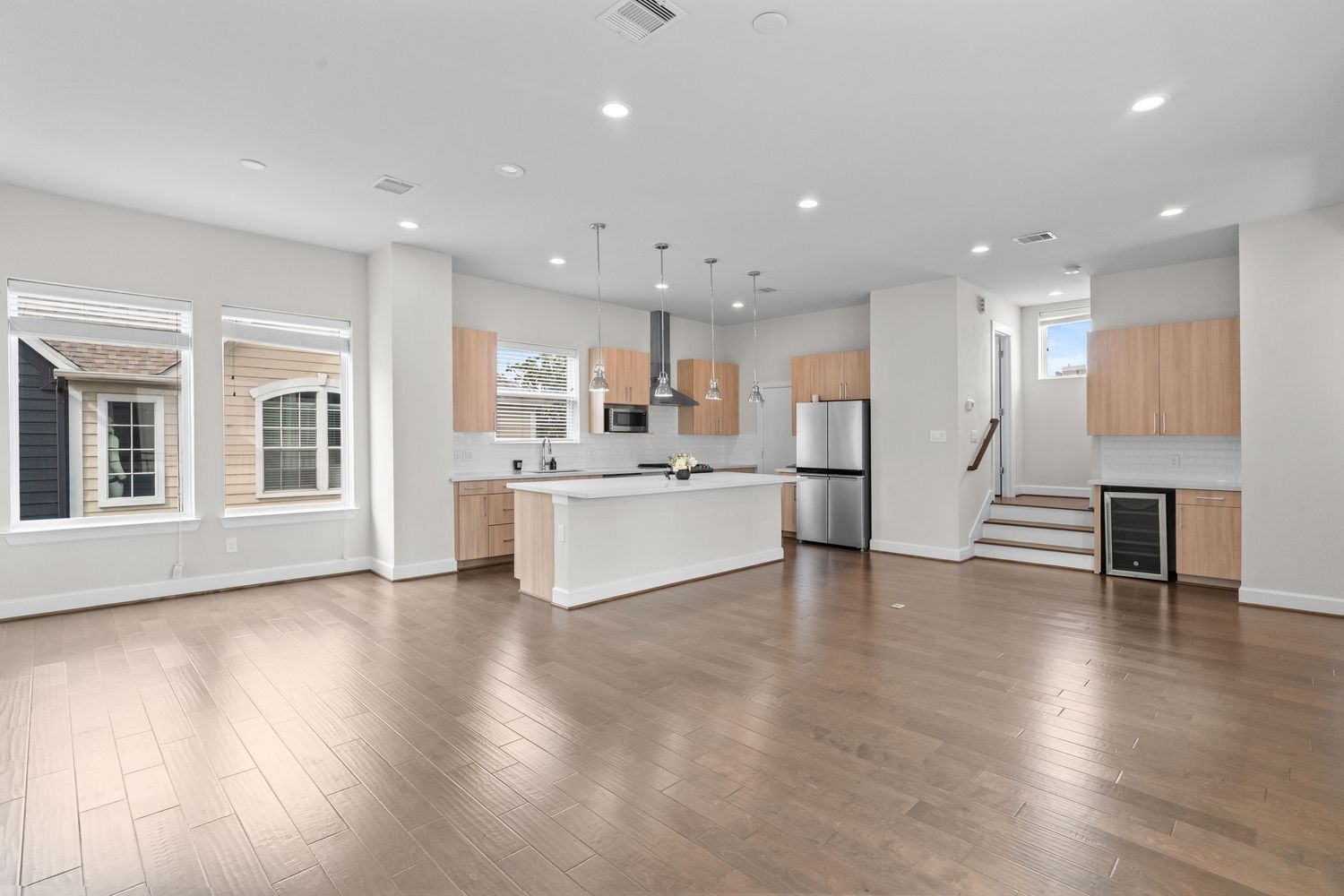 Modern open concept living space with hardwood floors, white kitchen island, and stainless steel appliances.