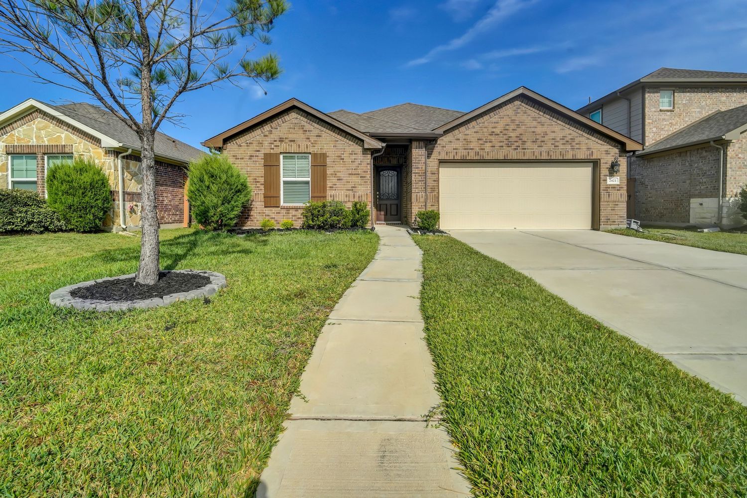 Modern brick ranch home with two-car garage and landscaped front yard featuring a curved concrete walkway.