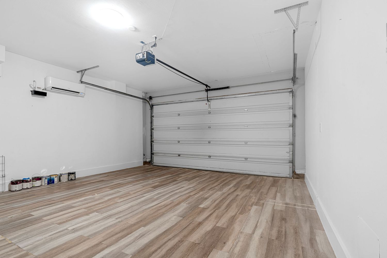 Interior view of an empty residential garage with white walls and light wood flooring.