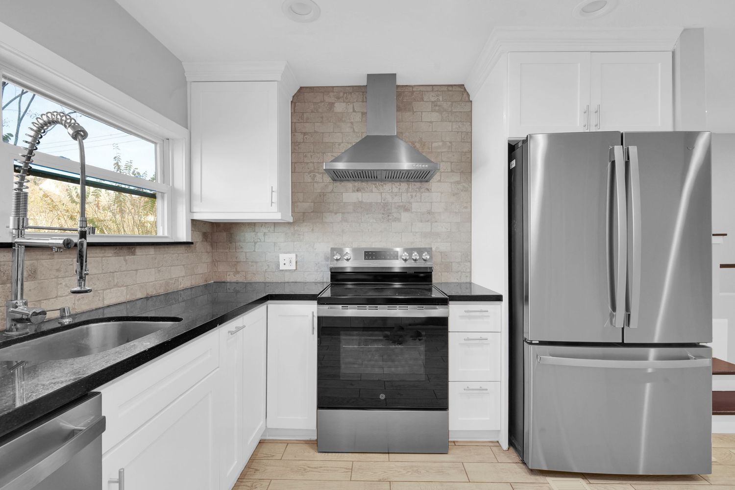 Modern kitchen with white cabinets, black countertops, stainless steel appliances and beige tile backsplash accent wall.