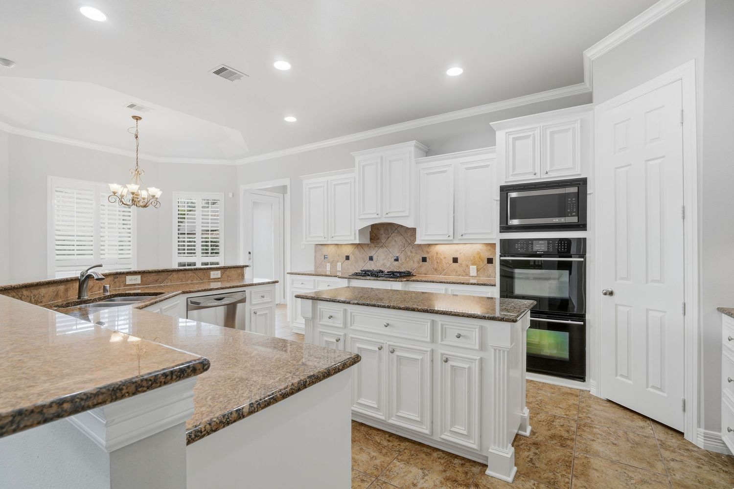 Modern white kitchen with granite countertops, recessed lighting, and pendant fixtures showcases clean lines and ample storage.
