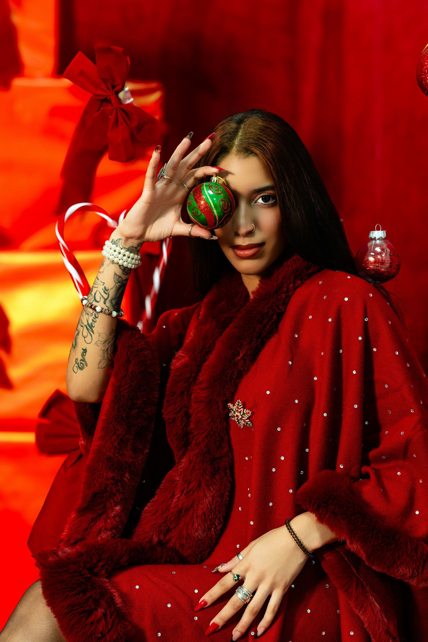 Woman in festive red outfit holding ornament in front of eye against red background with holiday decorations. Powerrpackmedia Houston Texas