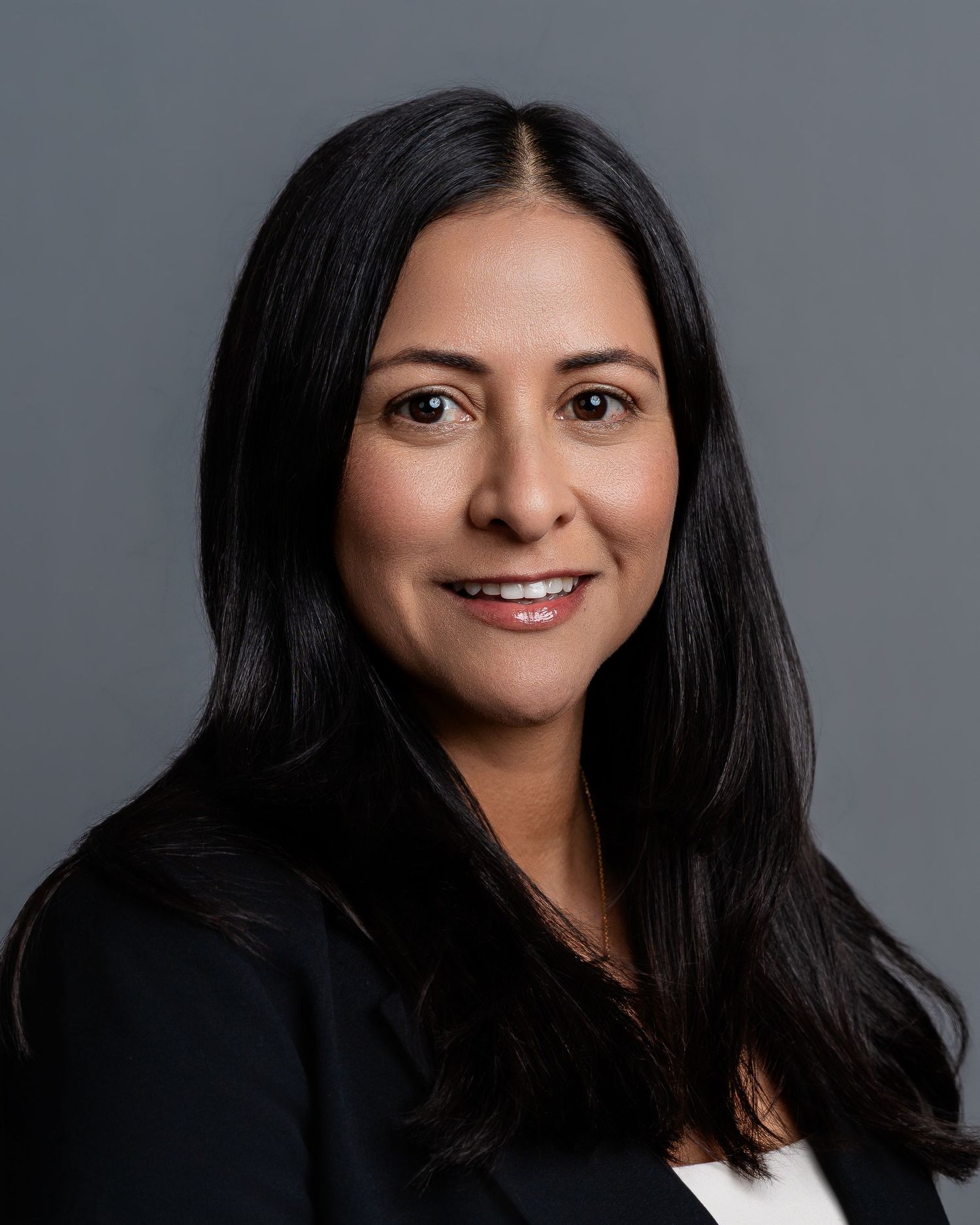 Professional headshot of a smiling woman with long dark hair wearing a black blazer against a gray background.