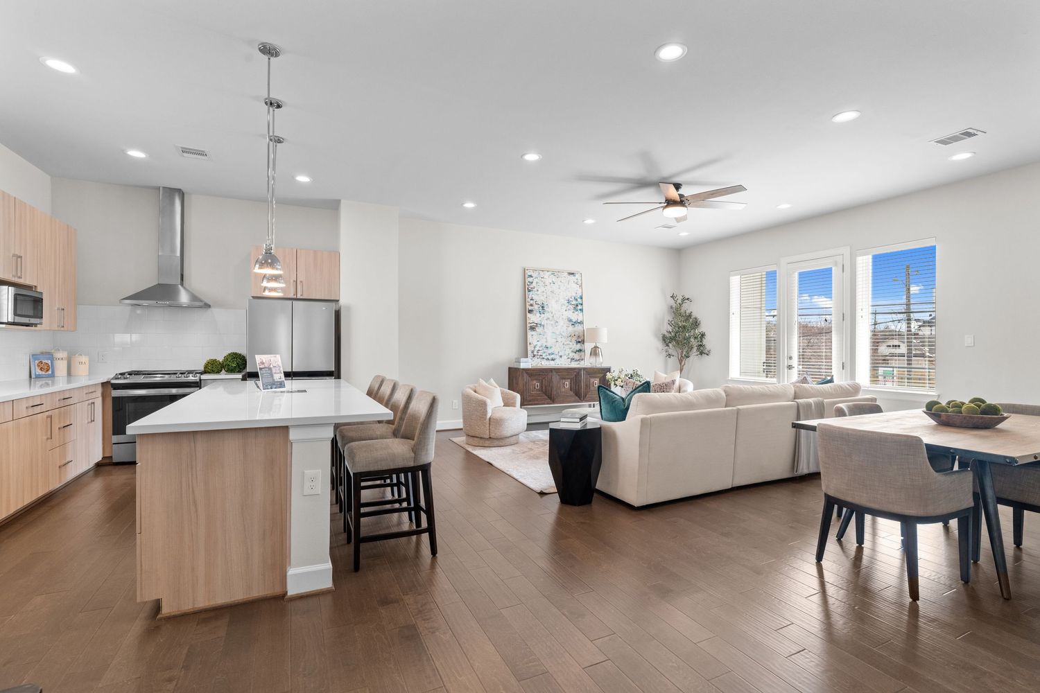 Modern open concept living space with white walls, recessed lighting, and light wood flooring throughout multiple rooms.