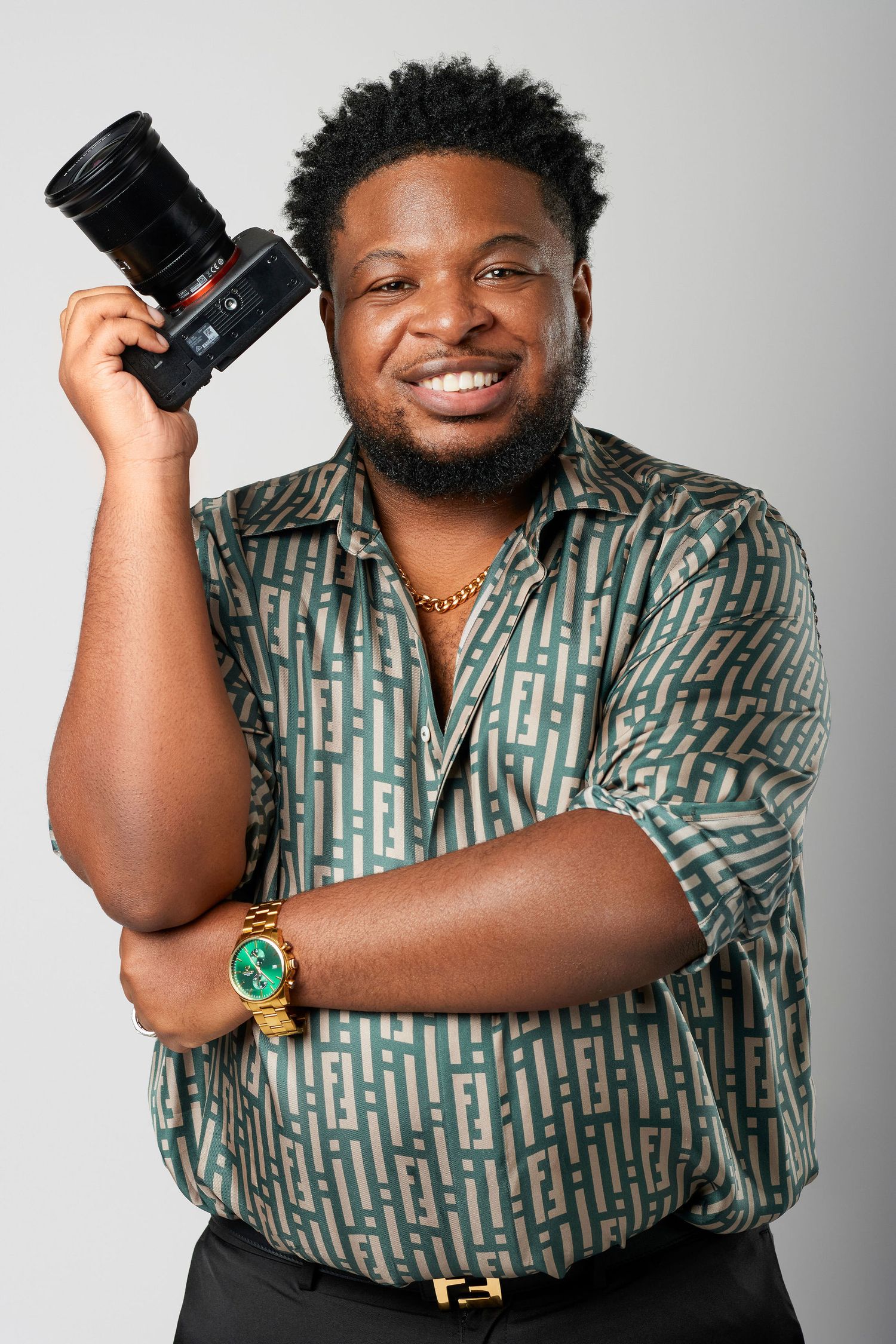 Cheerful photographer in geometric pattern shirt holds up professional camera against light background. Powerrpackmedia Houston Texas