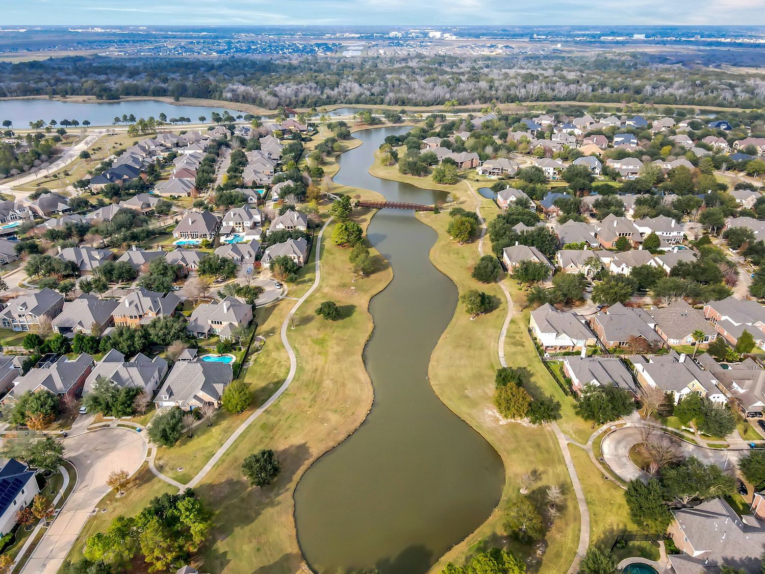 Aerial panoramic view of residential neighborhoods surrounding a winding lake with green spaces and walking paths.
