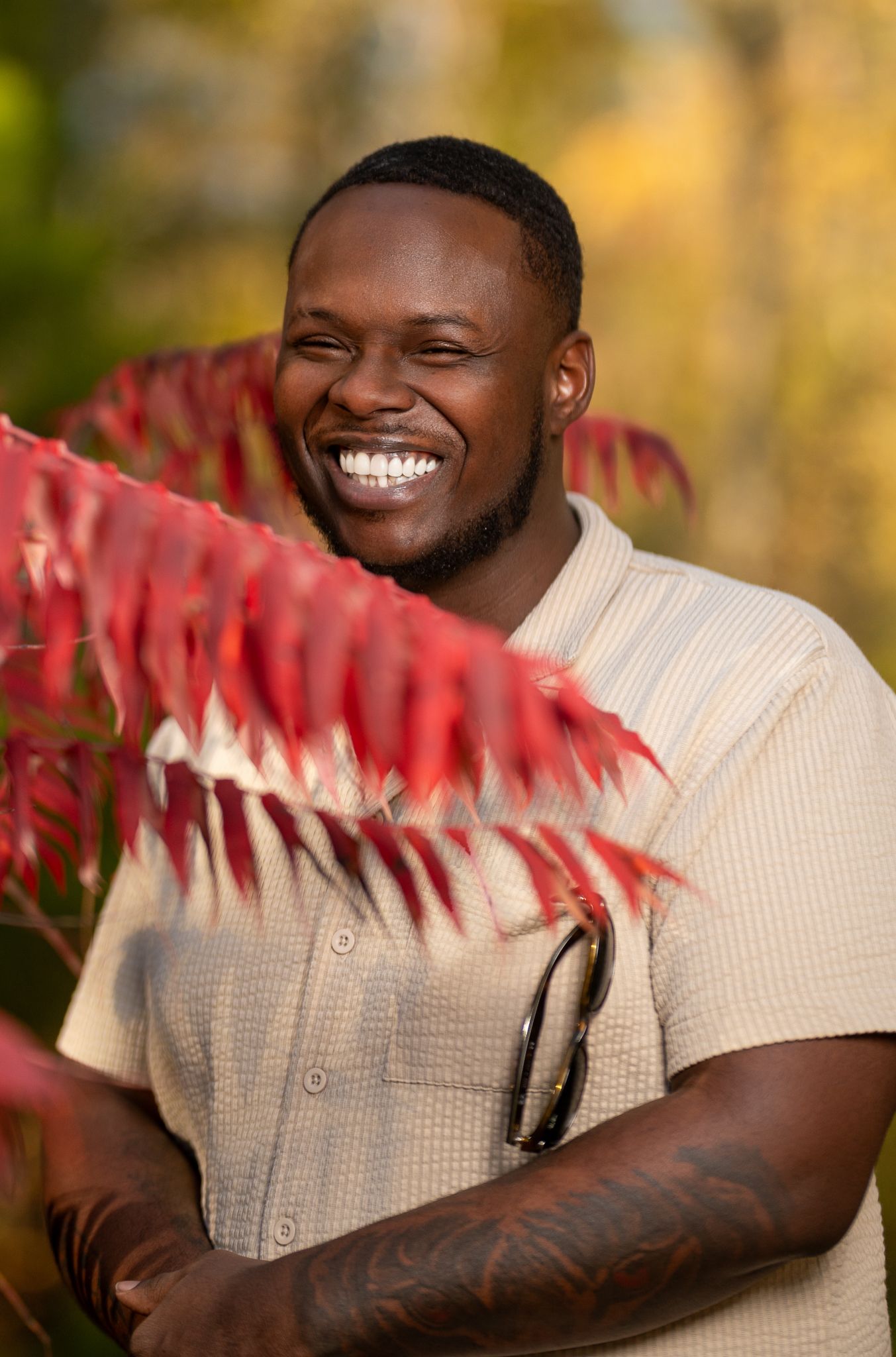 A person in a cream sweater poses outdoors with red autumn foliage in a series of expressive portraits. Powerrpackmedia Houston Texas