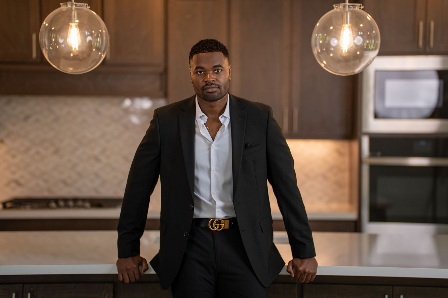 Person in business attire leaning on kitchen counter with pendant lights overhead. Powerrpackmedia Houston Texas