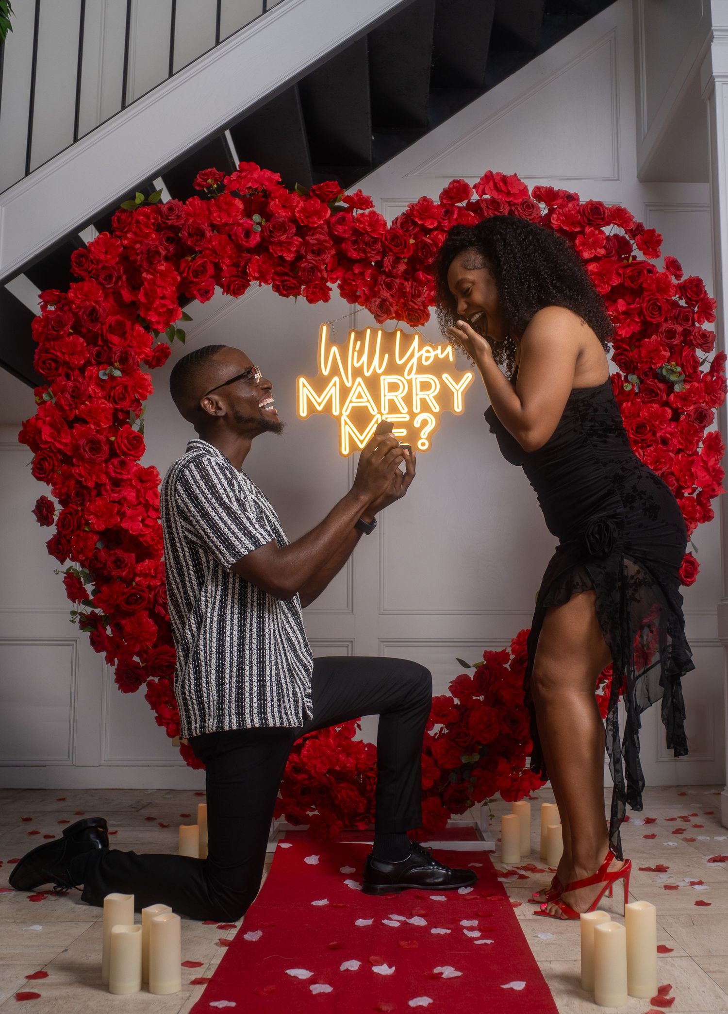 Marriage proposal scene with red roses and candles against a white backdrop with illuminated sign. Powerrpackmedia Houston Texas
