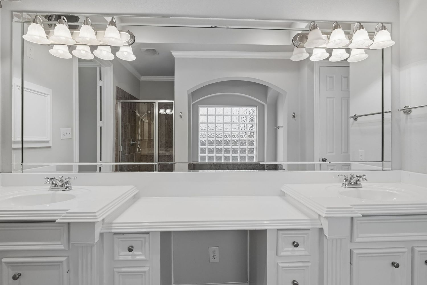 A modern white kitchen features a range hood, glass-front cabinets, and track lighting mounted above the counters.
